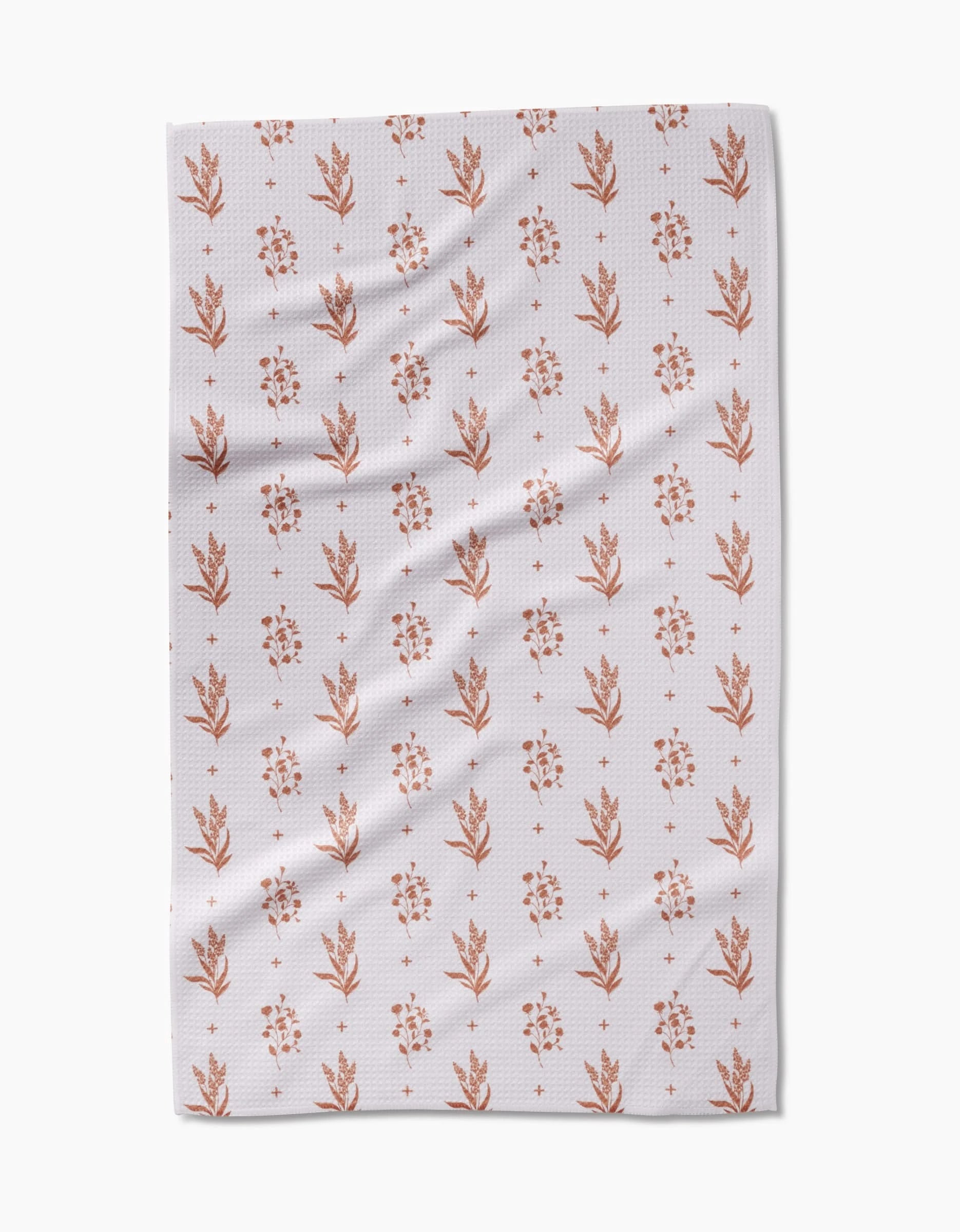 The Country Road tea towel by Charlie Rowan Designs is made from white Geoweave fabric and features a repeating pattern of small, rust floral and leaf motifs arranged in vertical rows. Subtle folds and creases are visible on the fabric.
