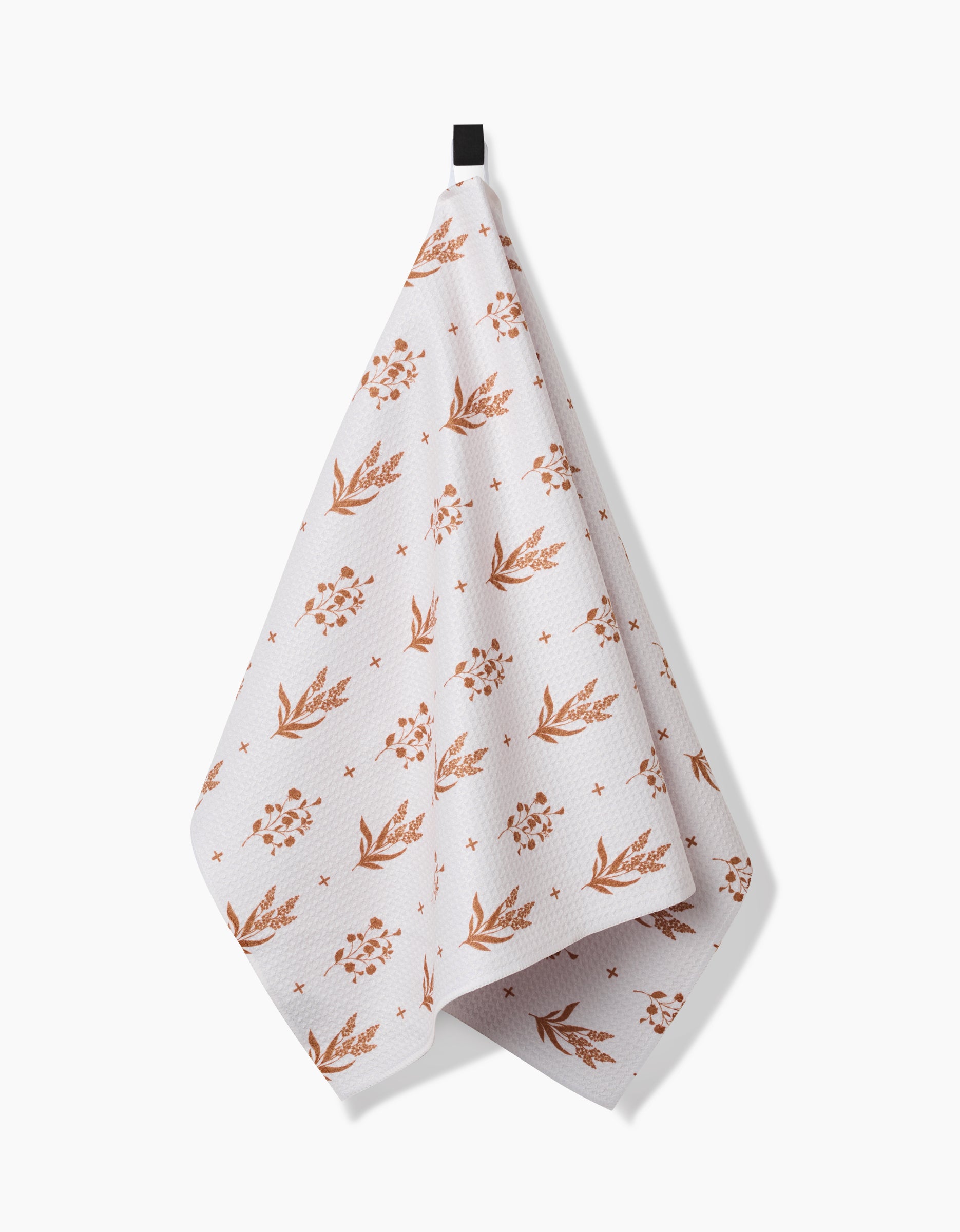 The Country Road tea towel by Charlie Rowan Designs features a rust floral and leaf pattern on soft, absorbent Geoweave fabric. It hangs from a black loop against a white background, showcasing its subtle textured design.