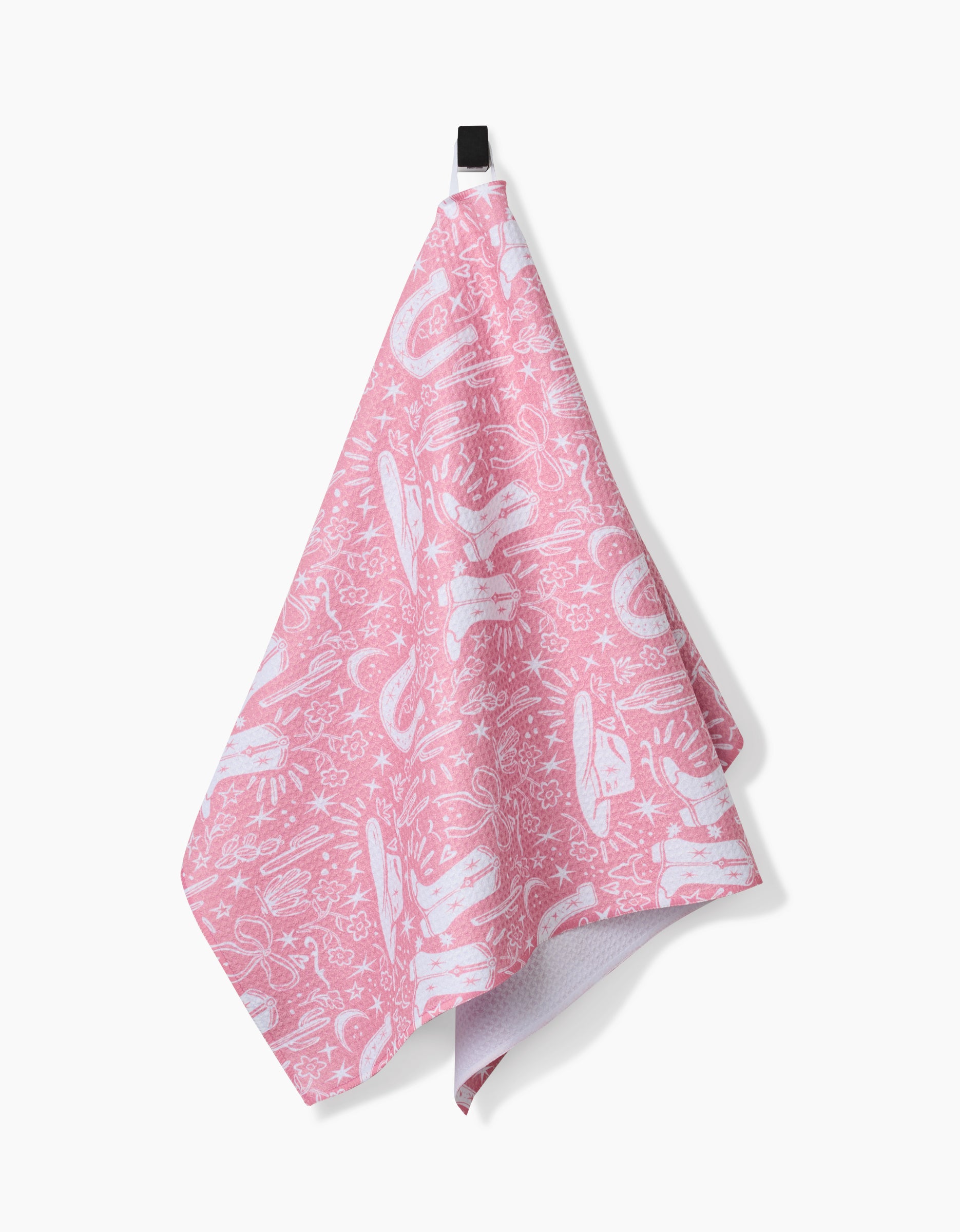 The Cowgirl Chic towel, featuring playful pink and white abstract patterns and made from ultra-absorbent Geoweave fabric, hangs from a black hook against a plain white background.