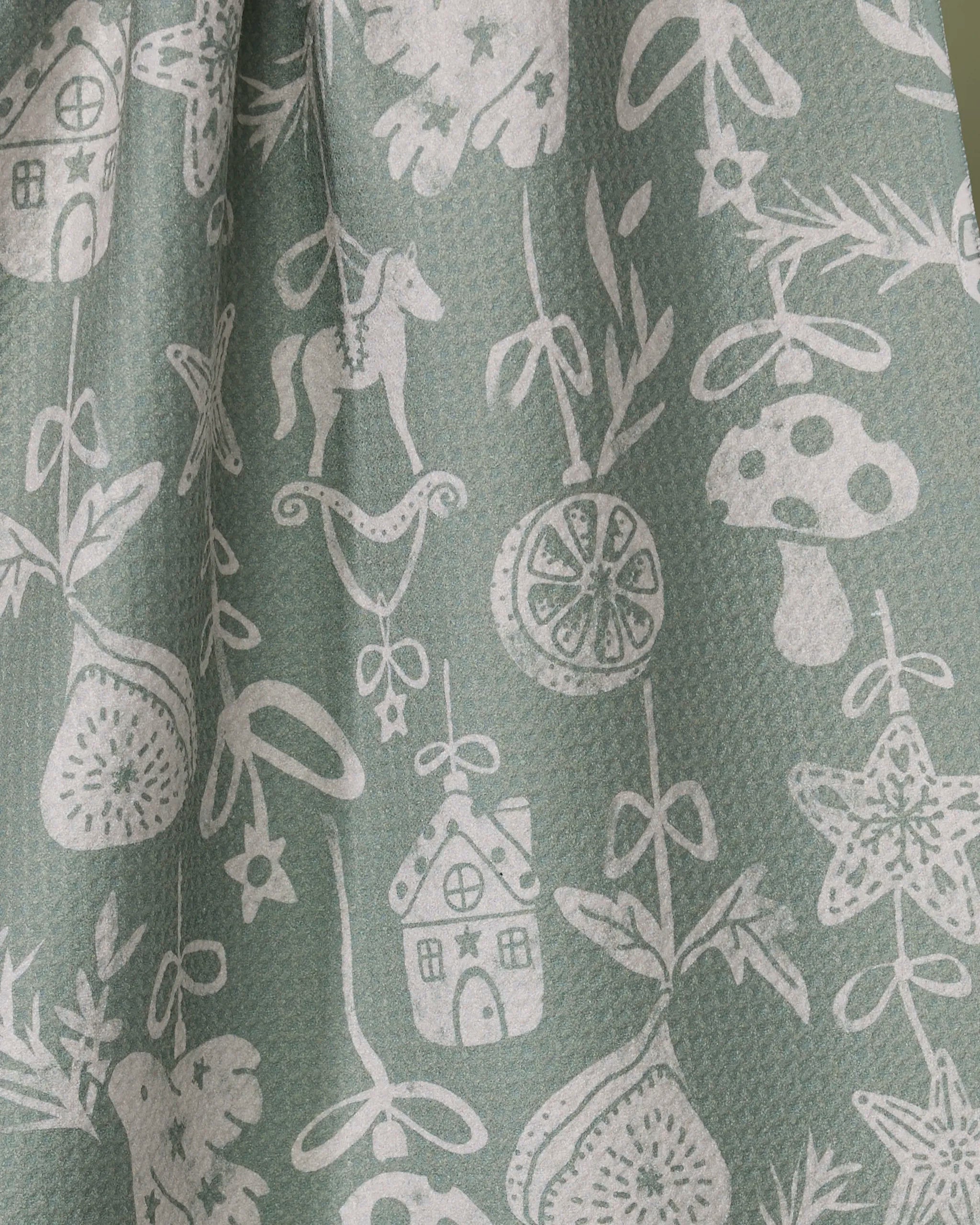 The Cozy Ornaments tea towel by Geometry features a whimsical white pattern of houses, horses, mushrooms, citrus slices, and plants on green. Ultra-absorbent and textured, it's a playful, nature-inspired accent for your kitchen.