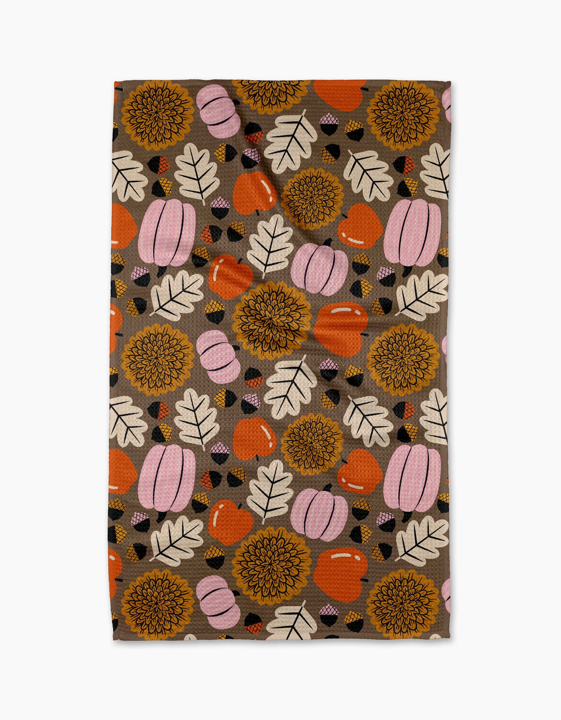 The "Crisp and Cozy" tea towel by Megan Roy features orange and pink pumpkins, yellow sunflowers, white leaves, and acorns on a brown background. Made from quick-drying recycled materials for eco-friendly autumn style.