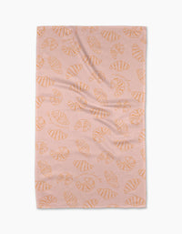 The Croissant Crush tea towel by Geometry, made from recycled materials, features orange croissants on pink and is shown laid flat against a white background.