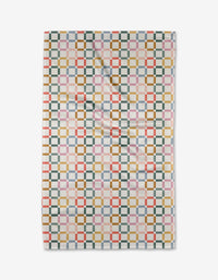 The Crossroads tea towel by Charlie Rowan Designs features a geometric pattern of interlocking squares in green, gold, red, blue, and pink on white Geoweave fabric, shown flat with slight folds.