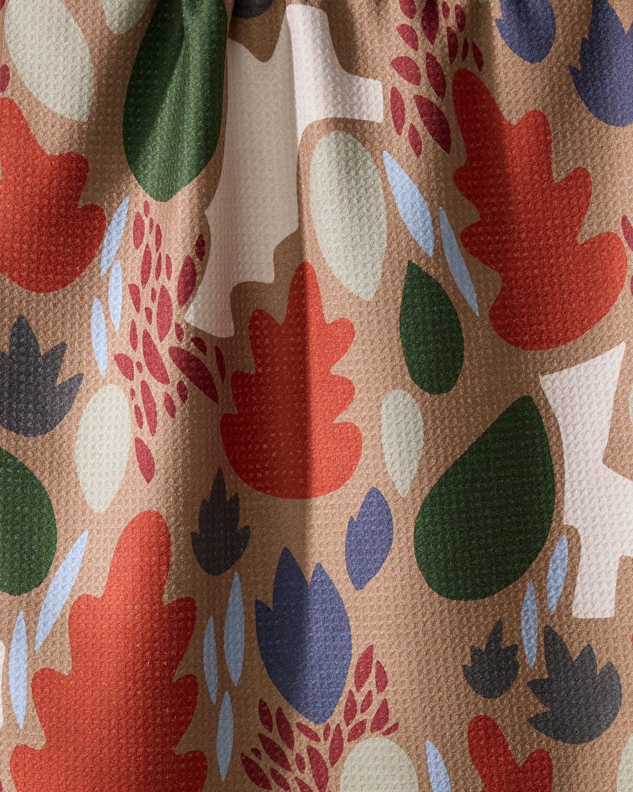 The Geometry Cut Paper Leaves Mocha dish towel features a colorful abstract leaf and floral pattern in red, green, blue, cream, and beige tones. Its absorbent, textured woven design adds playful charm to any kitchen.