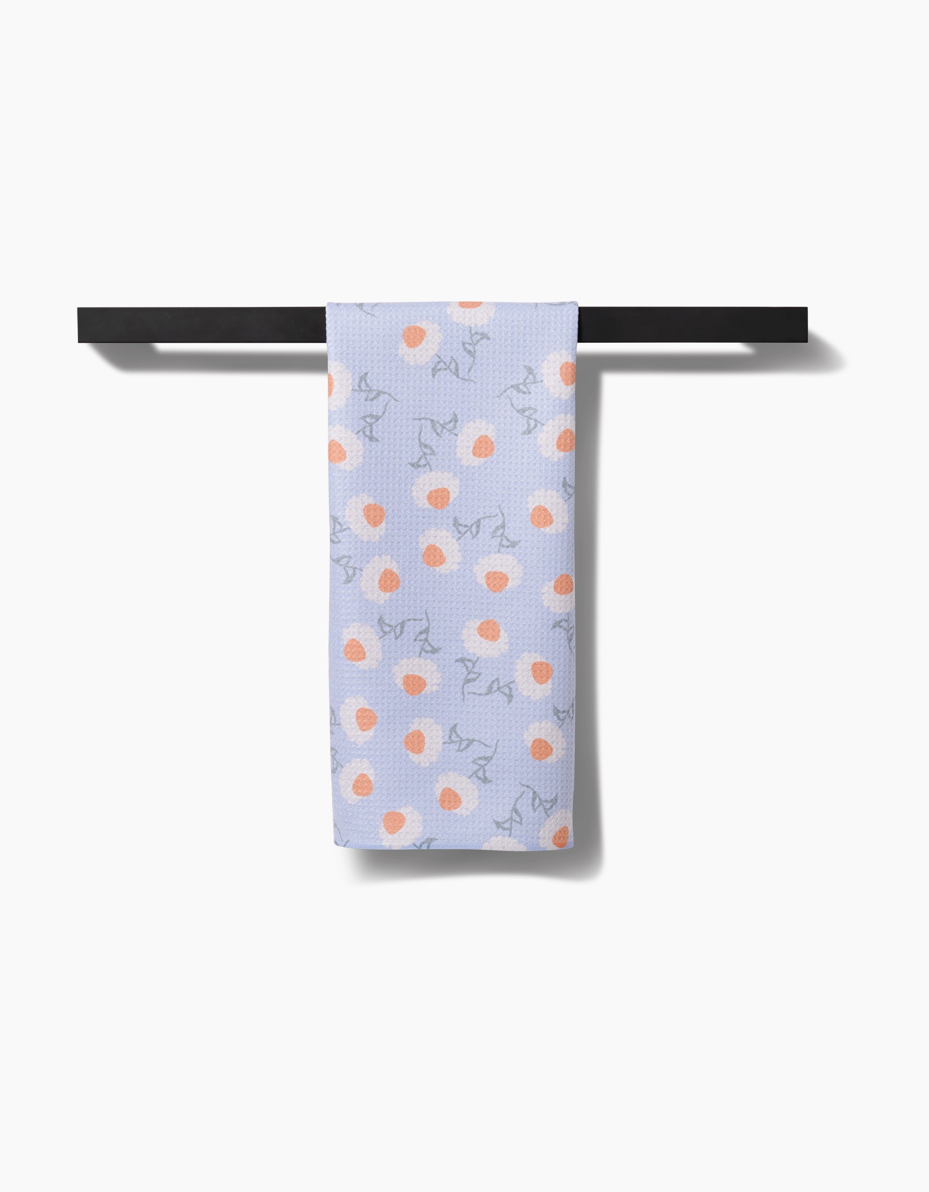 The Daisy Duets tea towel by Sarah Reed, made of light purple Geoweave fabric with peach and orange spots and blue line drawings, hangs neatly on a black towel bar against a white background.