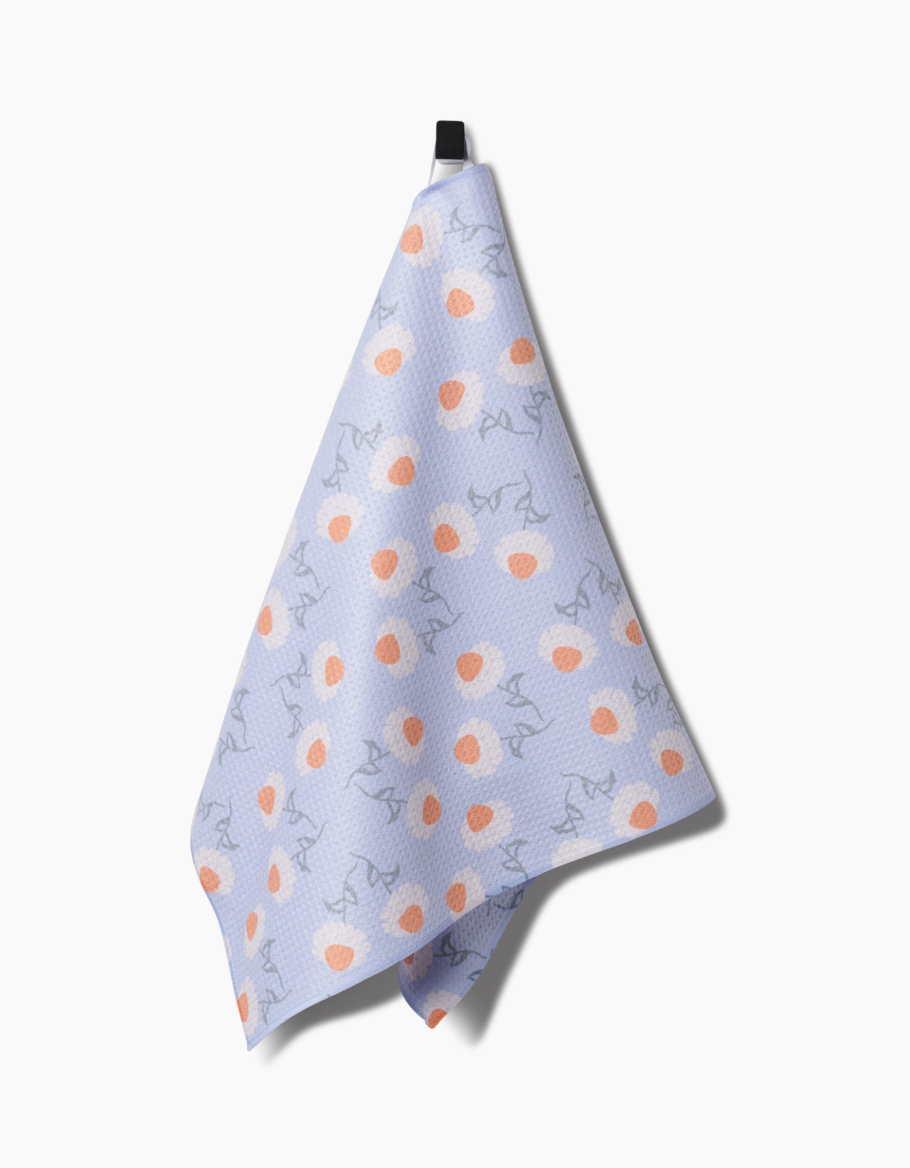 The Daisy Duets tea towel by Sarah Reed, made of lavender Geoweave fabric, features orange circles and grey squiggly lines, and hangs from a black loop against a plain white background.