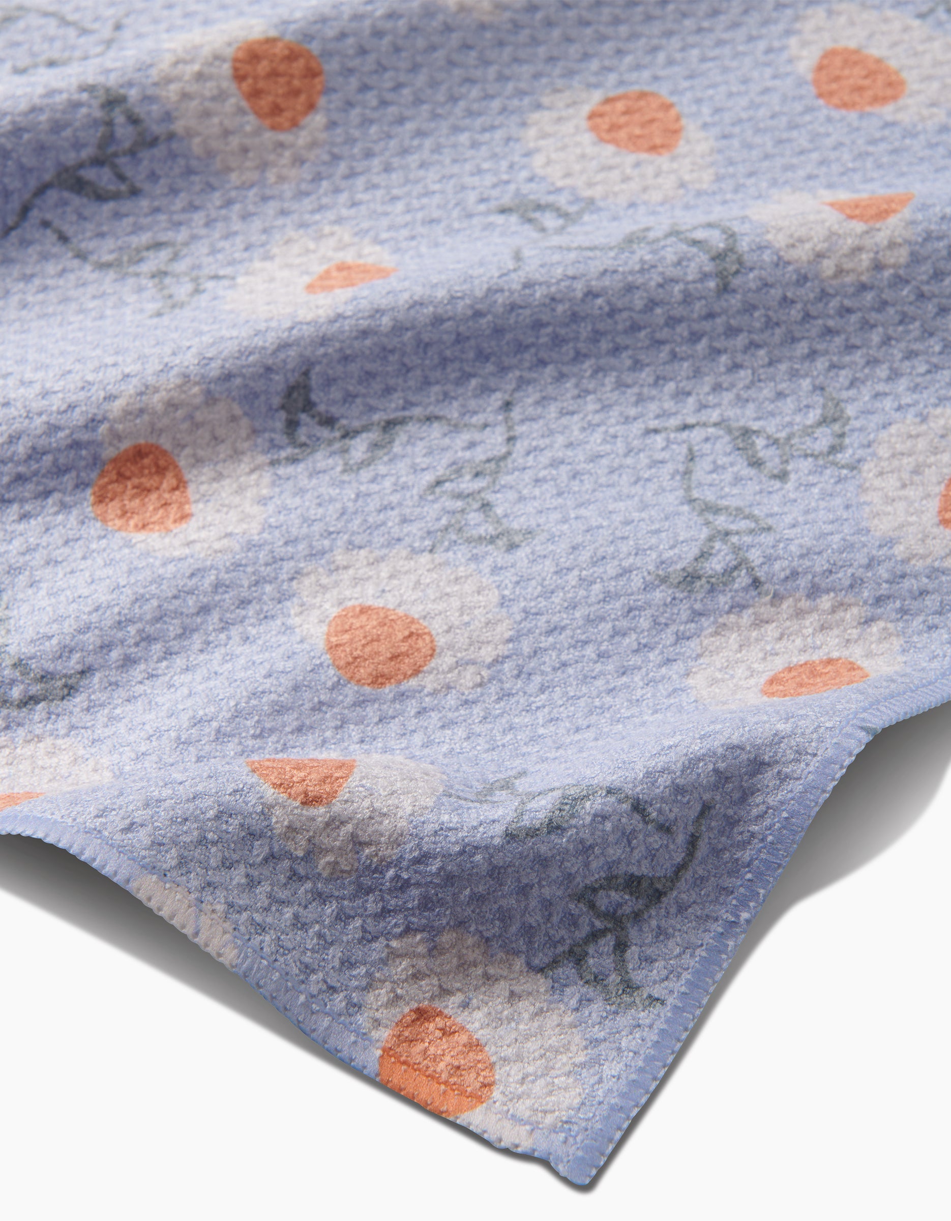 The Daisy Duets tea towel by Sarah Reed features light blue Geoweave fabric with a white daisy pattern, orange centers, and green stems. Slightly wrinkled and shown close up, it’s perfect for adding charm to your kitchen.