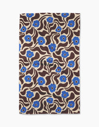 The Gerdadzy Dancing Blooms tea towel features a beige background with blue flowers, wavy brown lines, and leaves in a bold, retro style. Made from recycled materials.