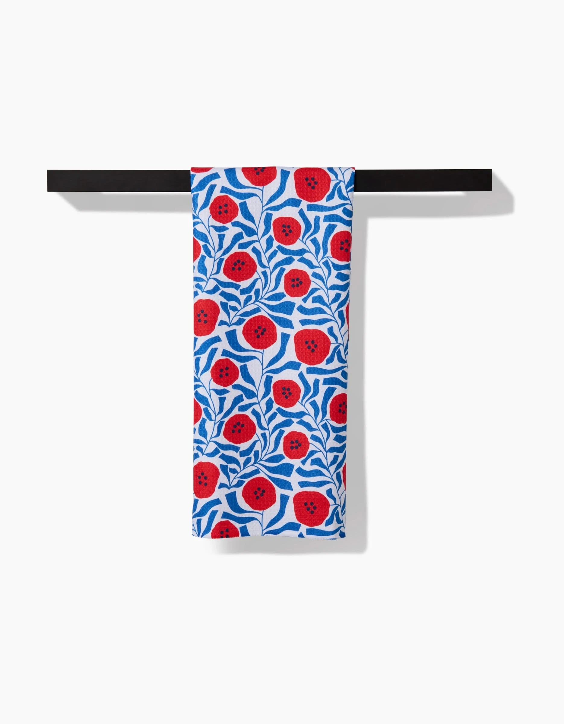The Dancing Poppies towel by Happy Hemera, crafted from ultra-absorbent Geoweave fabric and featuring a vibrant red and blue floral pattern, hangs neatly over a horizontal black bar against a white background.