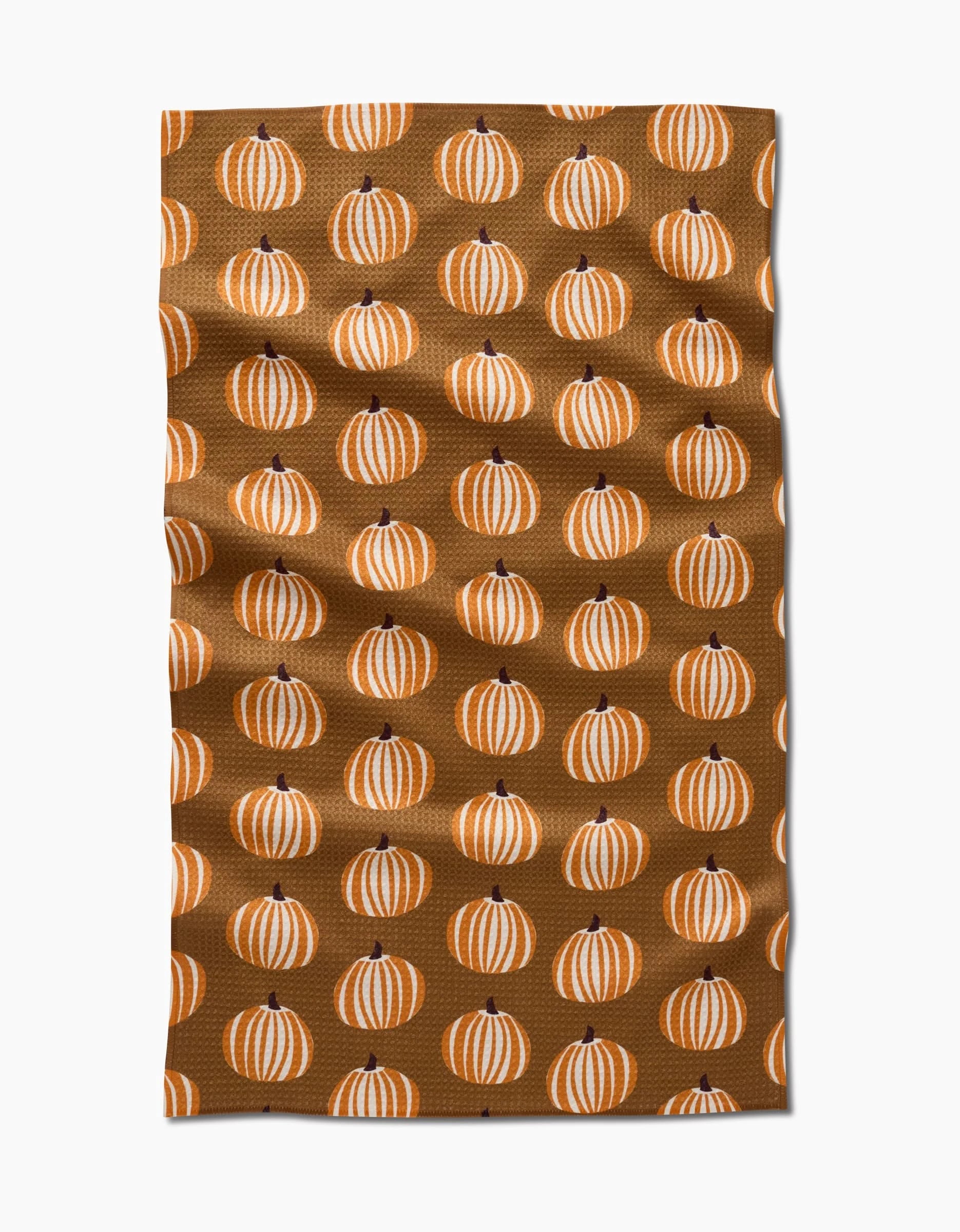 The Dancing Pumpkins tea towel by Lizzie Clark features orange and white striped pumpkins in a repeating pattern on brown, bringing festive autumn charm to your kitchen.