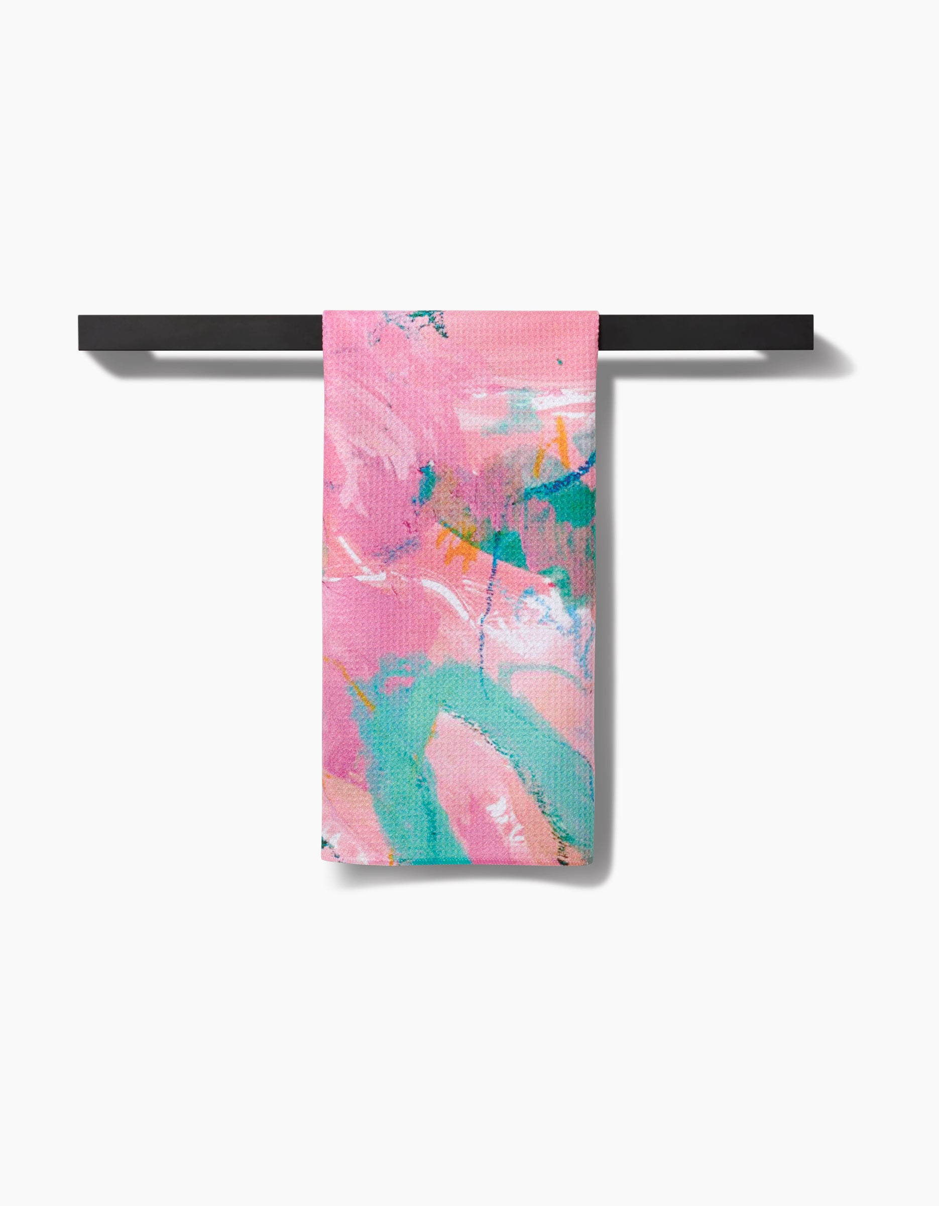 The Daughter hand towel by Sarah Holden, made from recycled materials, features abstract pink, teal, orange, and white brushstroke patterns and is shown folded over a black bar on a white background.