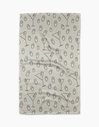 The Dirty Martini tea towel by Rosa Kichline showcases a beige textured background with a repeating pattern of green martini glasses and olives evenly scattered across the surface.