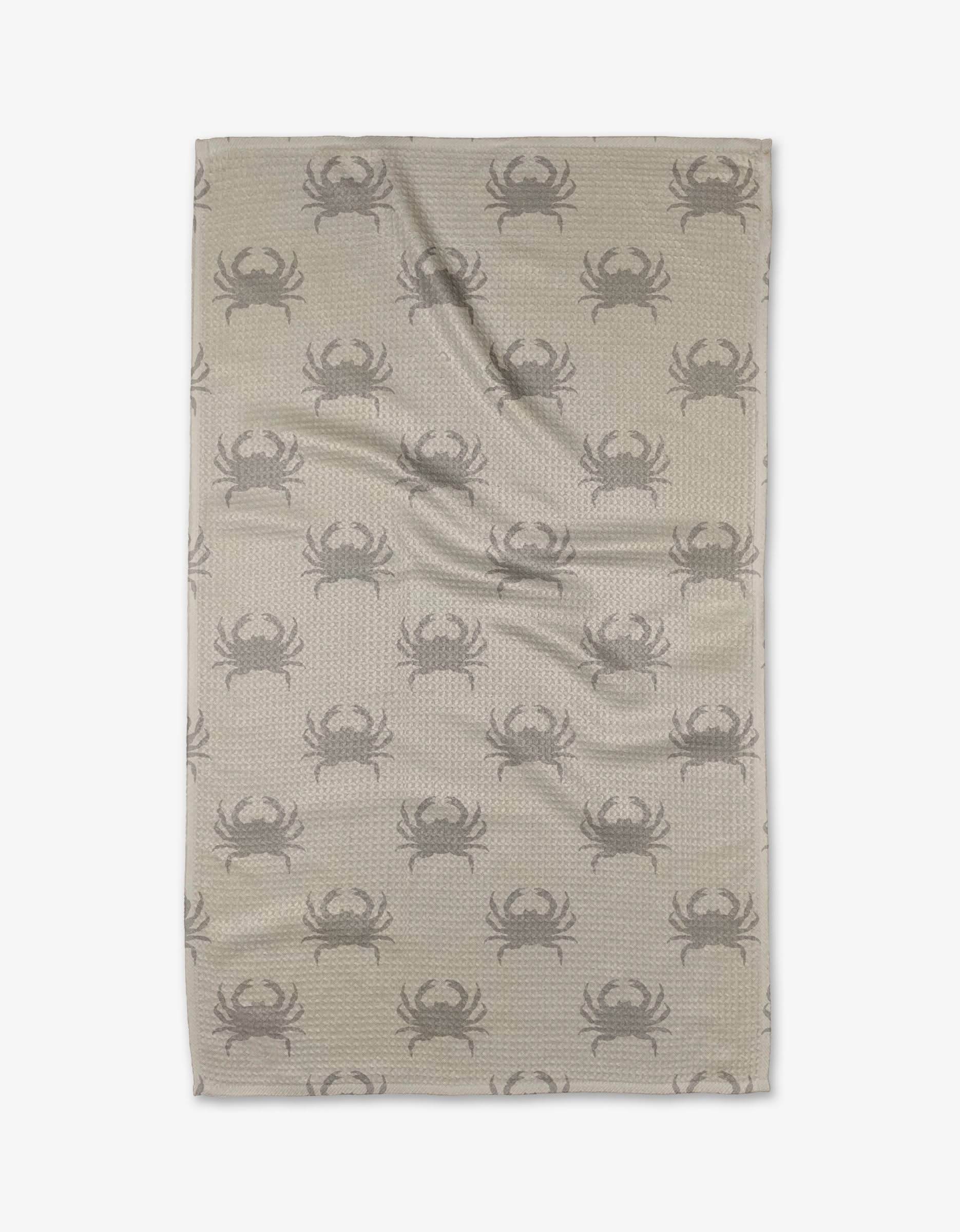 The Dungeness Days tea towel by Jenny Keller features a beige backdrop with a repeating dark gray crab pattern. Made from quick-drying, recycled materials for eco-friendly convenience. Shown flat with slight wrinkles on a white background.