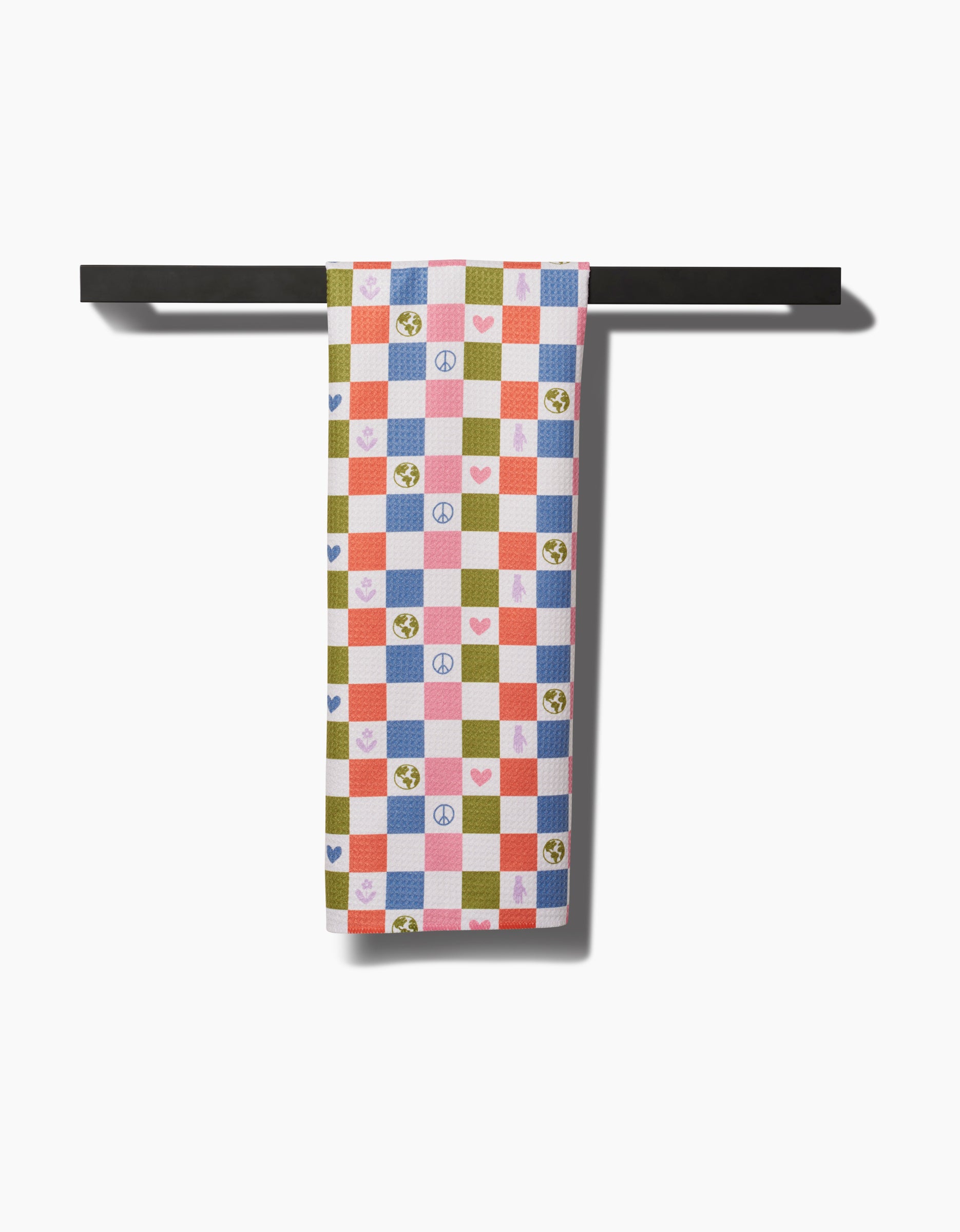 The Kayla Ann Earth Day Checkers Kitchen Tea Towel features a colorful checkered pattern with blue, red, and green squares, peace signs, hearts, and Earth symbols. Made from recycled materials, it hangs neatly on a black rod.