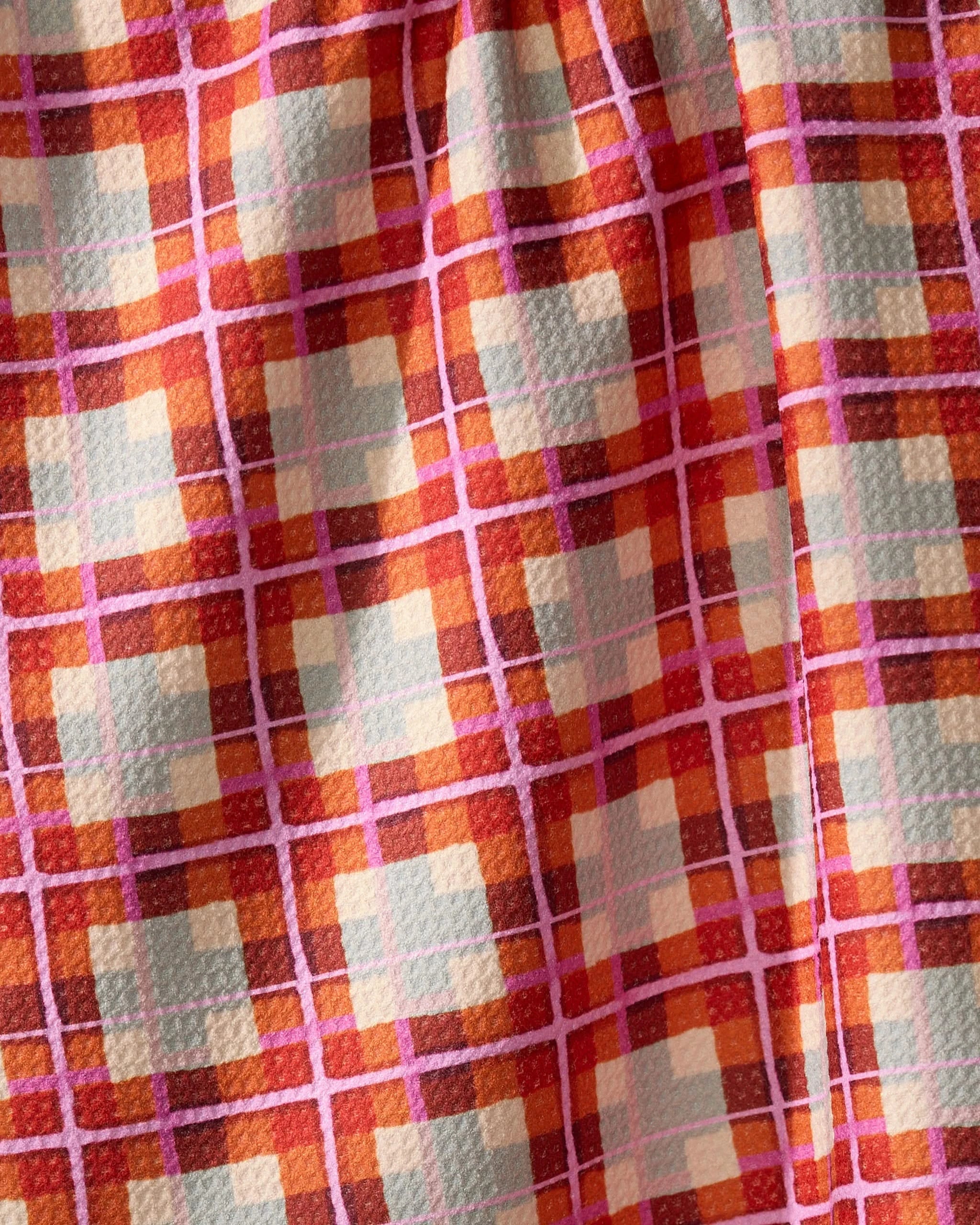 A close-up of Geometrys Ecstatic For Autumn recycled kitchen towel shows its colorful plaid pattern in orange, red, yellow, and pink. The ultra-absorbent towel features a soft, textured surface with gentle folds.