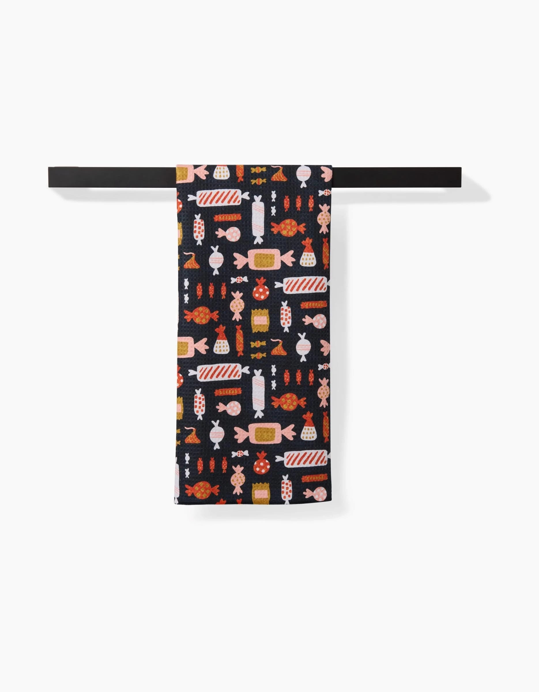 The Edwina Tea Towel by Amy MacCready, crafted from recycled materials, displays a vibrant candy pattern in orange, red, pink, and white. It hangs neatly on a black bar against a white background.