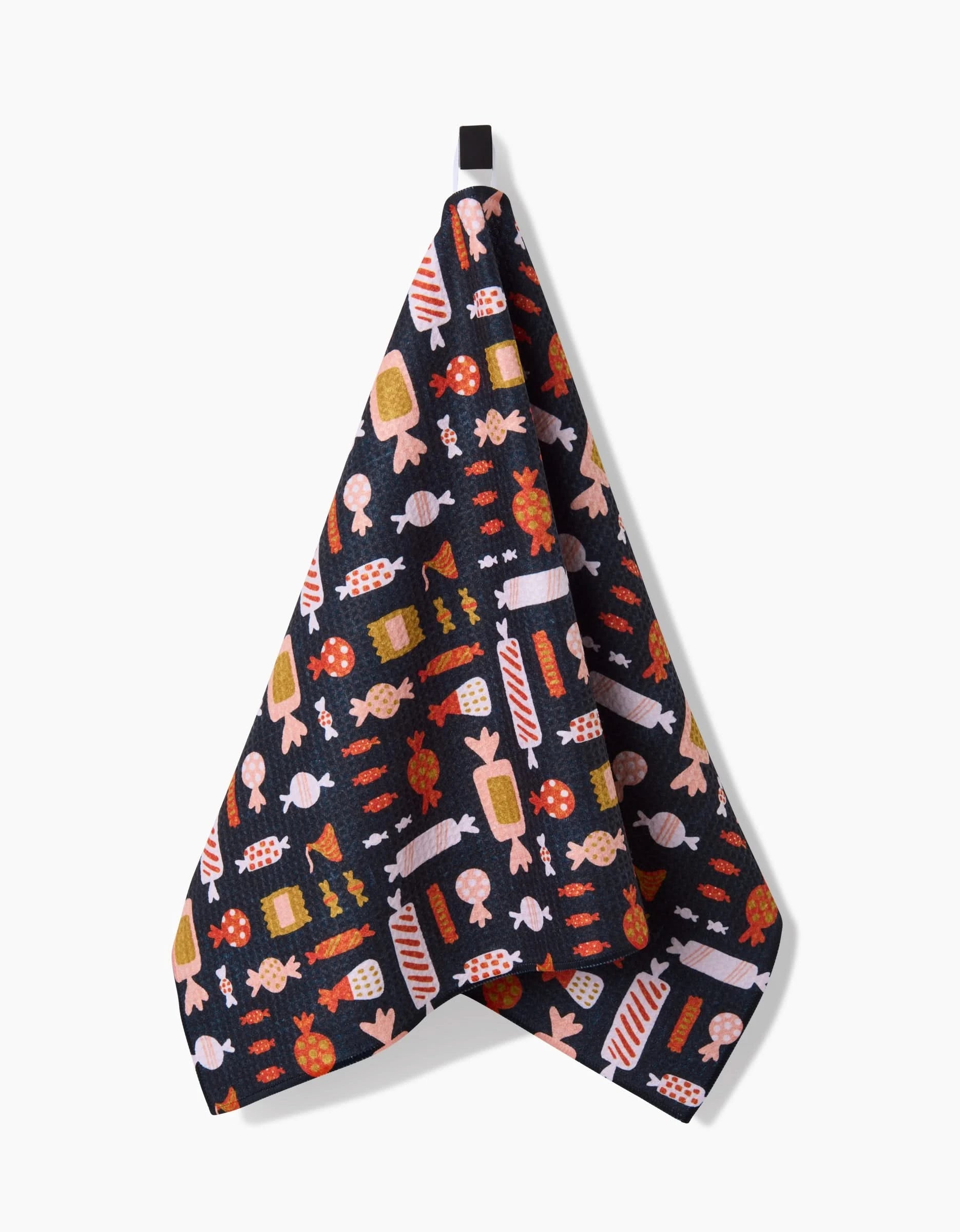 The Edwina tea towel by Amy MacCready is black, made from recycled materials, and features playful candy illustrations in red, pink, orange, and yellow. It hangs from a loop against a white background.