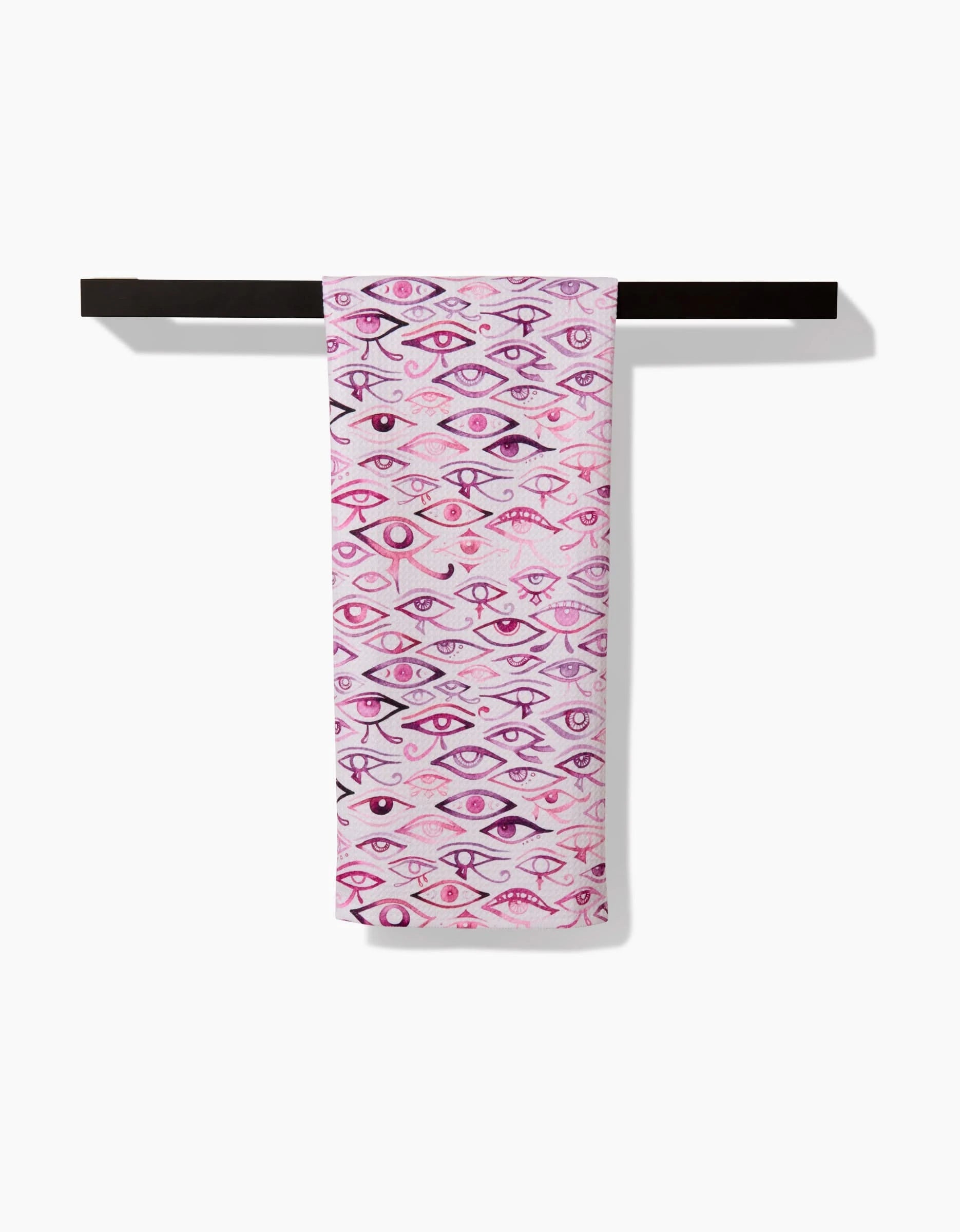 The Eye Of Horus tea towel by Maayan Alper-Swan, crafted from recycled materials, features illustrated eyes in pink and purple tones. It hangs on a black rod against a white background.