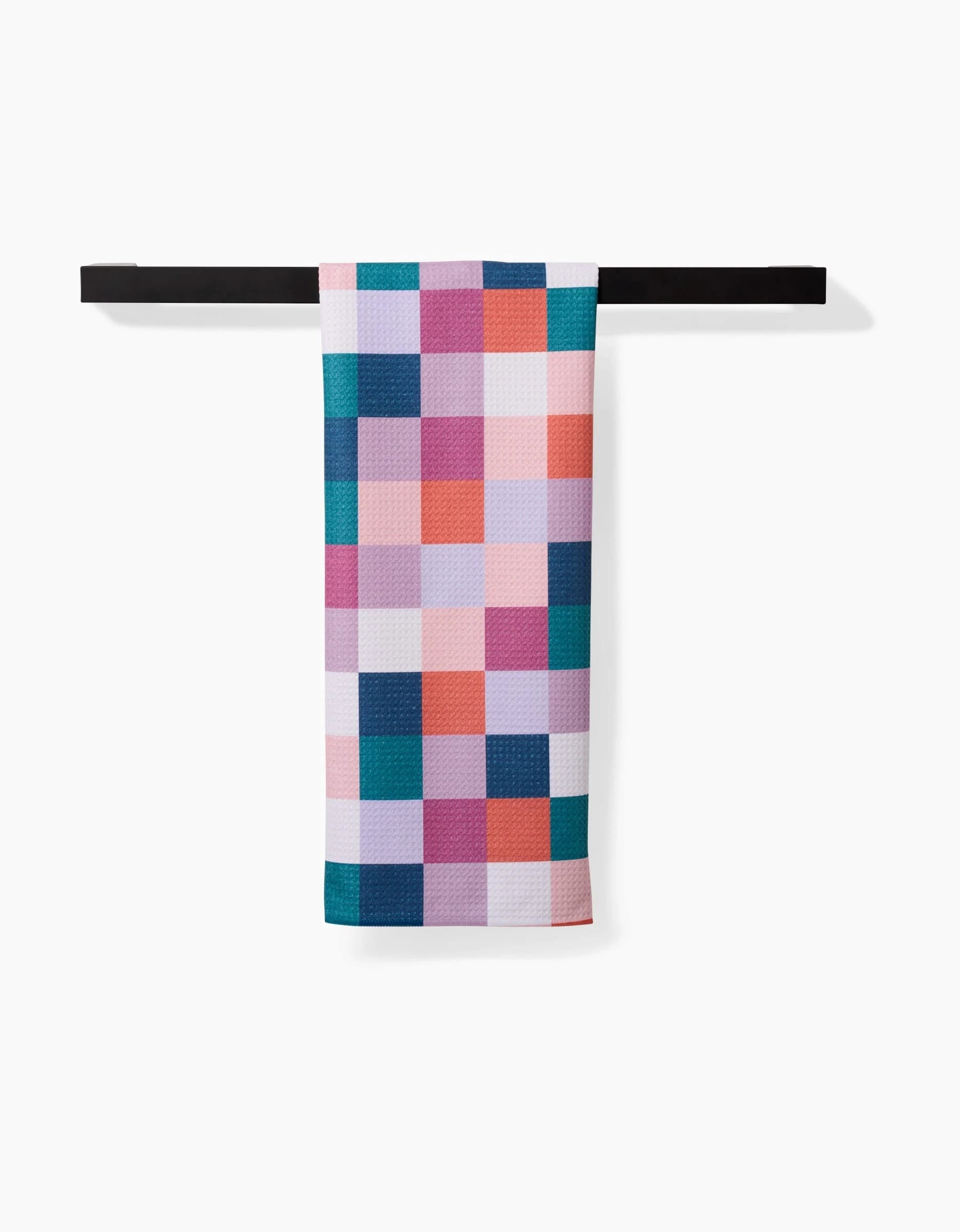The Fall Checkers tea towel by Claire Iglesias, featuring a vibrant blue, pink, purple, and orange checkered pattern, hangs neatly folded on a black bar. Crafted from durable Geoweave fabric and displayed against a white background.