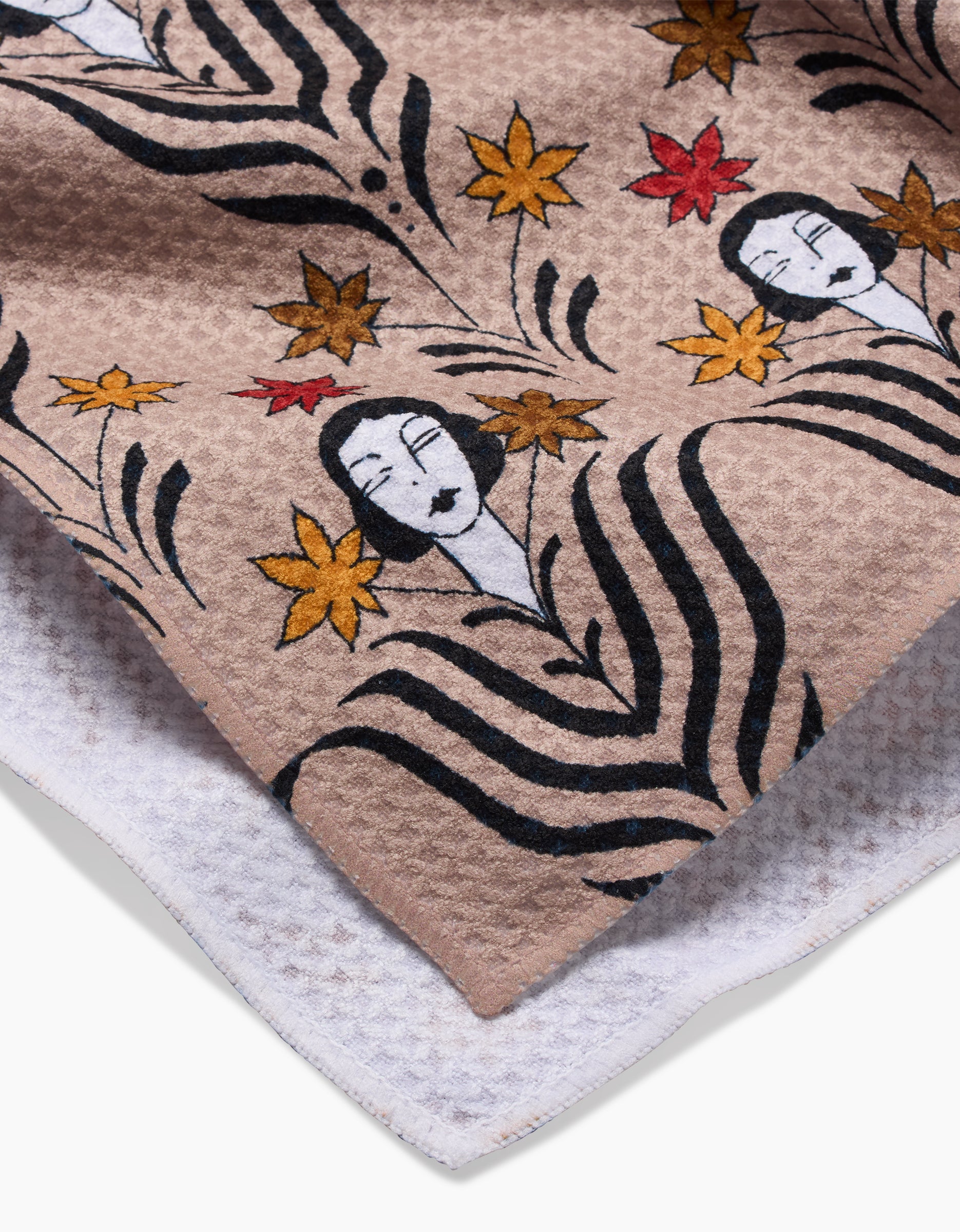 A close-up of Cole Strems Fall Deco Dame tea towel, showing its textured Geoweave fabric with an artistic pattern of stylized womens faces, black and white geometric lines, and red, yellow, and orange maple leaves.