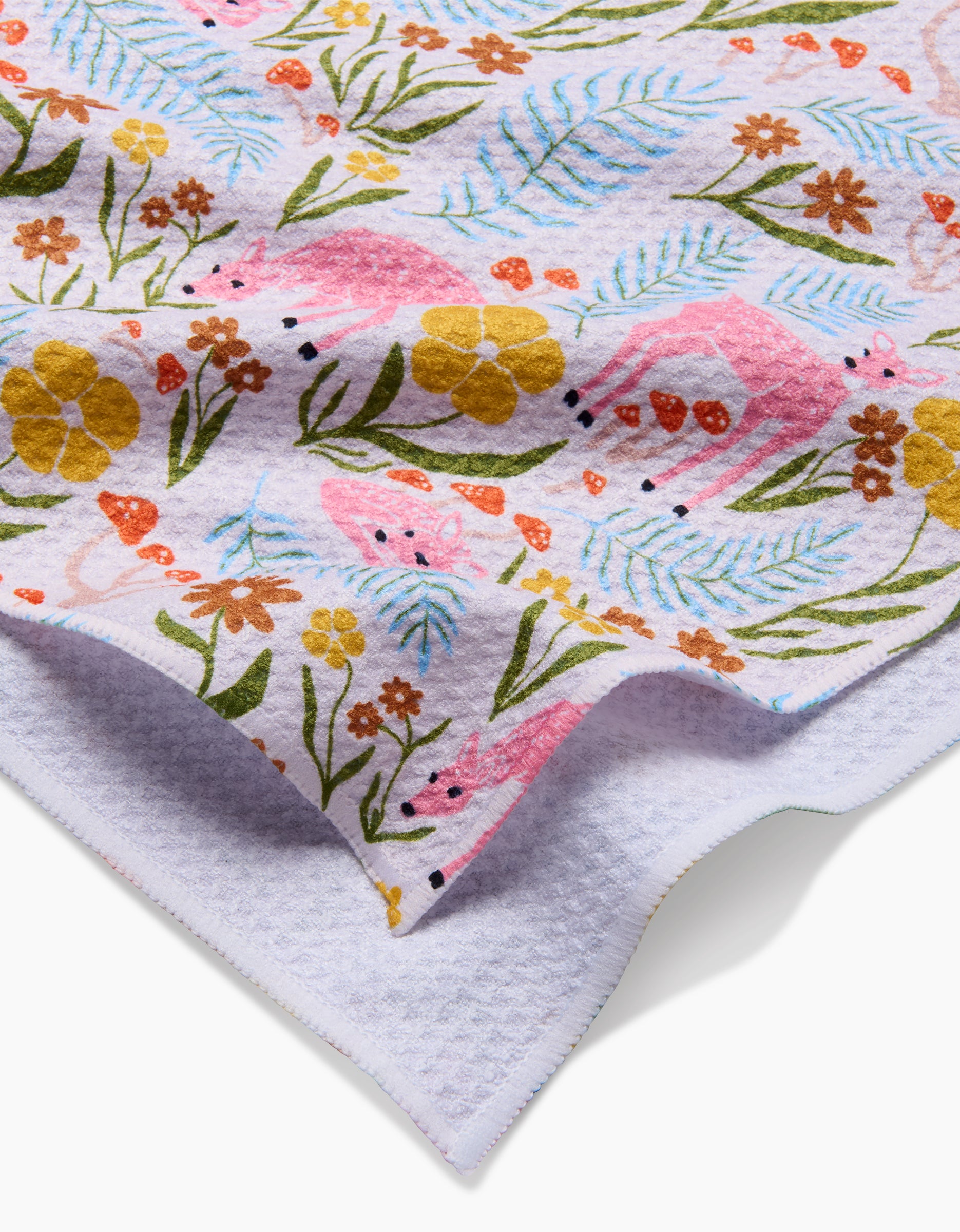 Close-up of the Fern and Fawn tea towel by Kayla Ann, made from white textured Geoweave fabric with colorful pink flamingos, yellow-orange flowers, and green leaves. The folded edge shows the underside crafted from recycled materials.