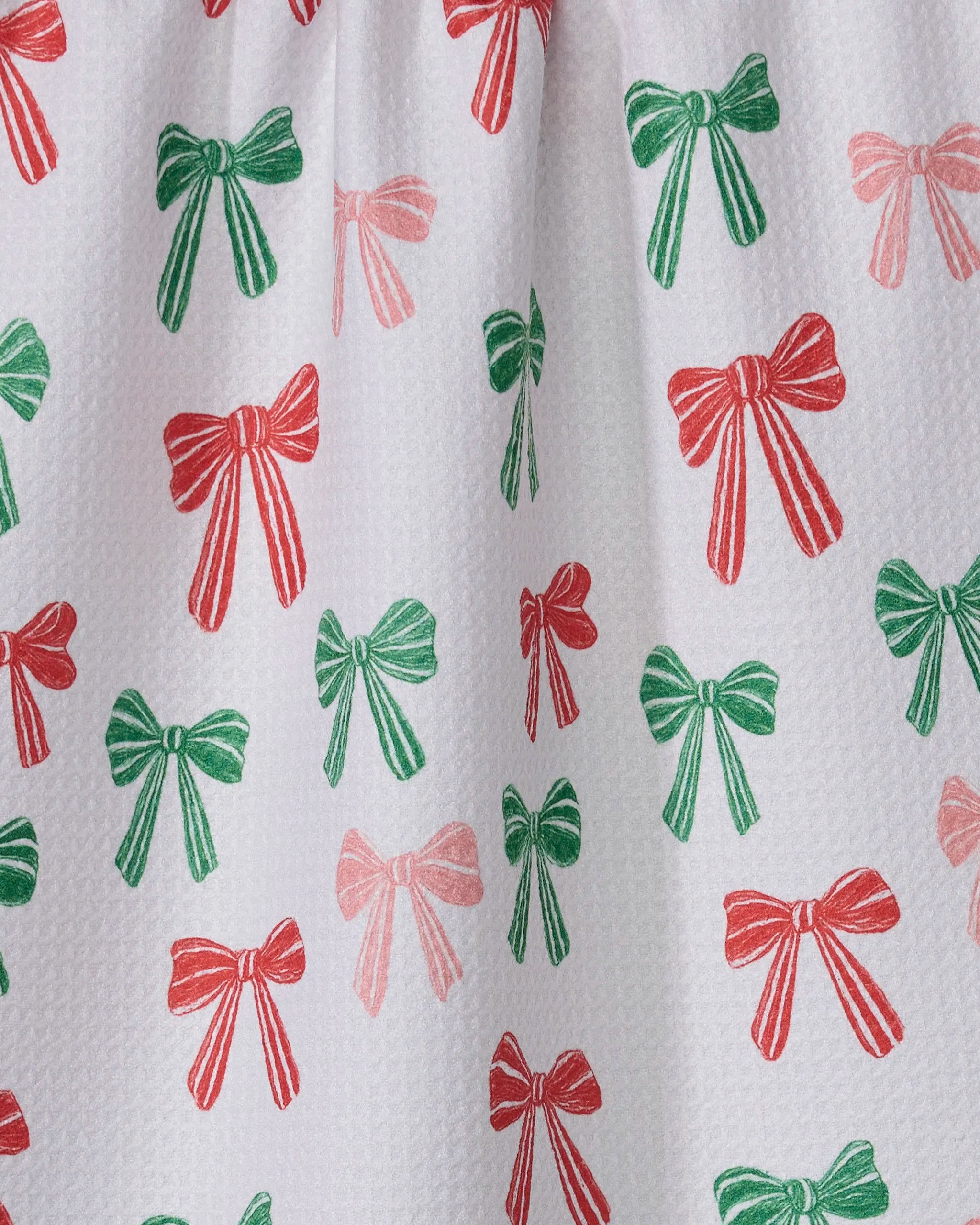A close-up of Geometry's Festoon recycled kitchen towel, showcasing white textured fabric adorned with a scattered, repeating design of red and green bows in various sizes.
