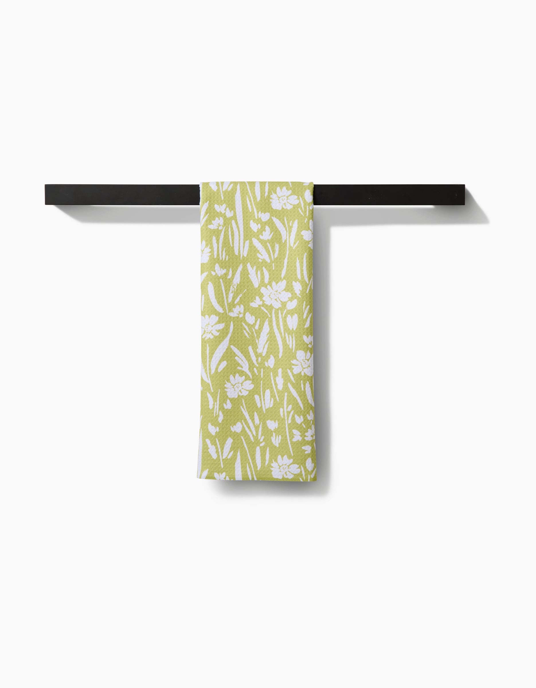 The Ashley Celena Field of Wildflowers towel, featuring a white floral pattern on light green ultra-absorbent Geoweave fabric, hangs neatly folded over a black horizontal bar against a plain white background.