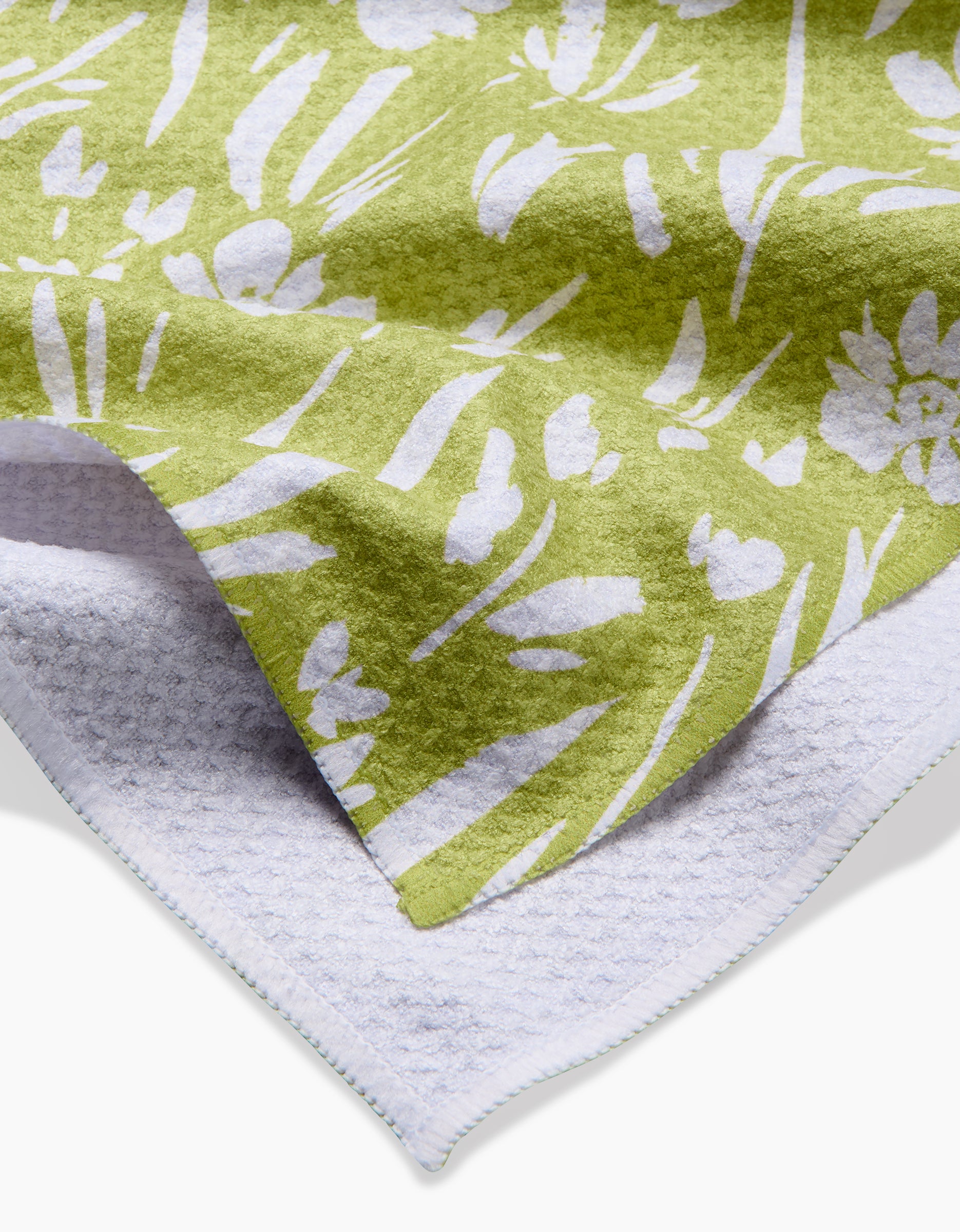 A close-up of the Ashley Celena Field of Wildflowers towel, showcasing a green and white floral pattern on one side with a textured, ultra-absorbent plain white underside.