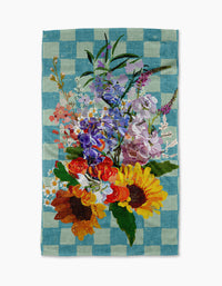 Add charm to your home with Pascale Dilger’s Flower Bouquet kitchen towel—a blue and white checkered, recycled towel featuring a central illustration of sunflowers, orange blooms, and purple wildflowers. Eco-friendly style!.