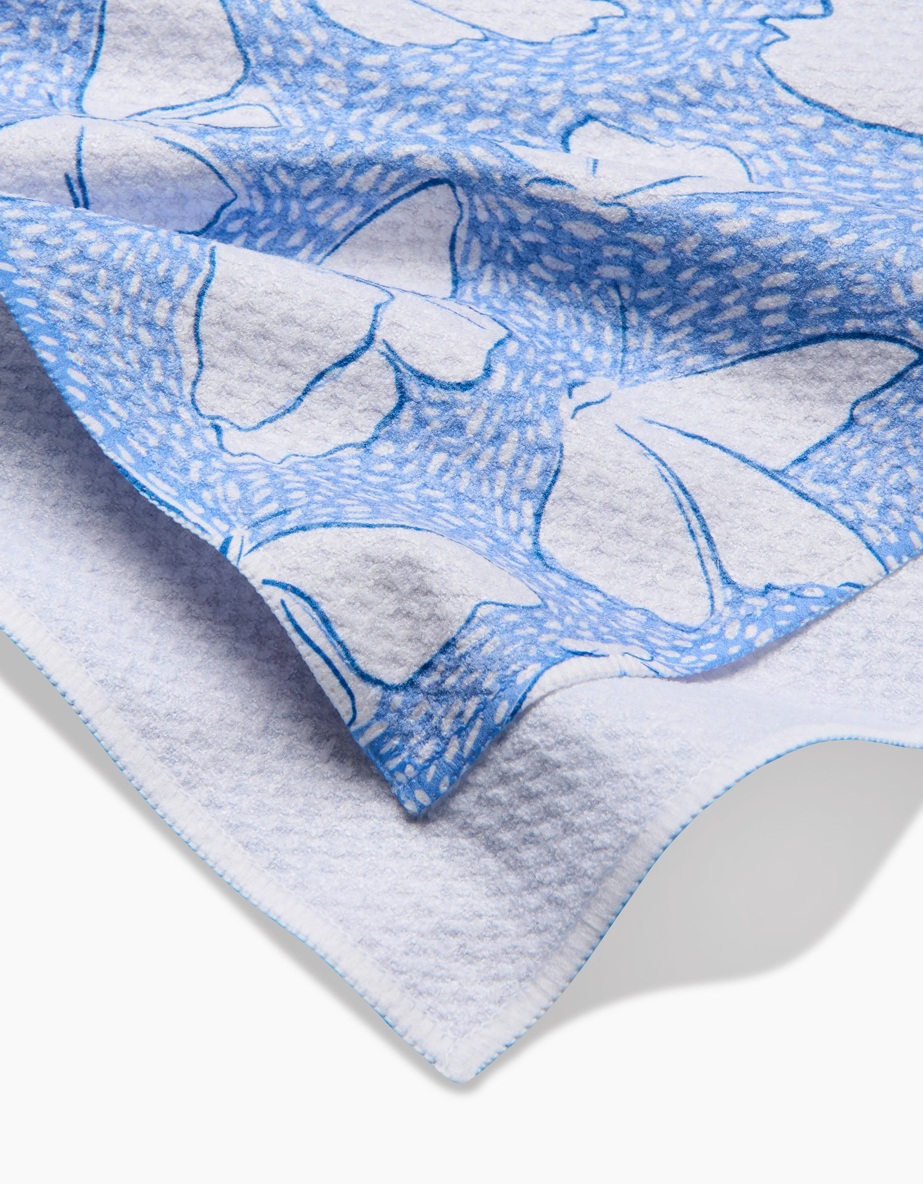 A close-up of the Fly Away Butterfly tea towel by Hufton Studio, showcasing its soft texture, blue butterfly pattern, and blue edge stitching on a white background.