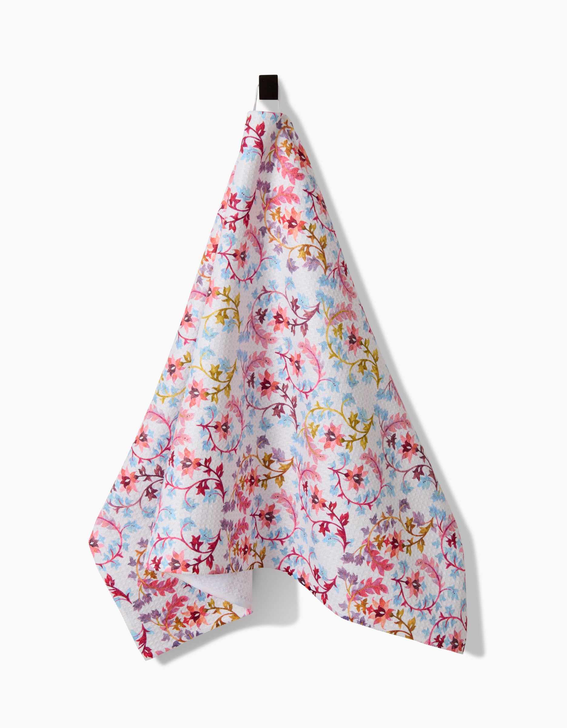 The Folk Tapestry kitchen towel by Maayan Alper-Swan features a vibrant floral design in pink, red, blue, and yellow on ultra-absorbent Geoweave fabric. It hangs from a black loop against a white background.