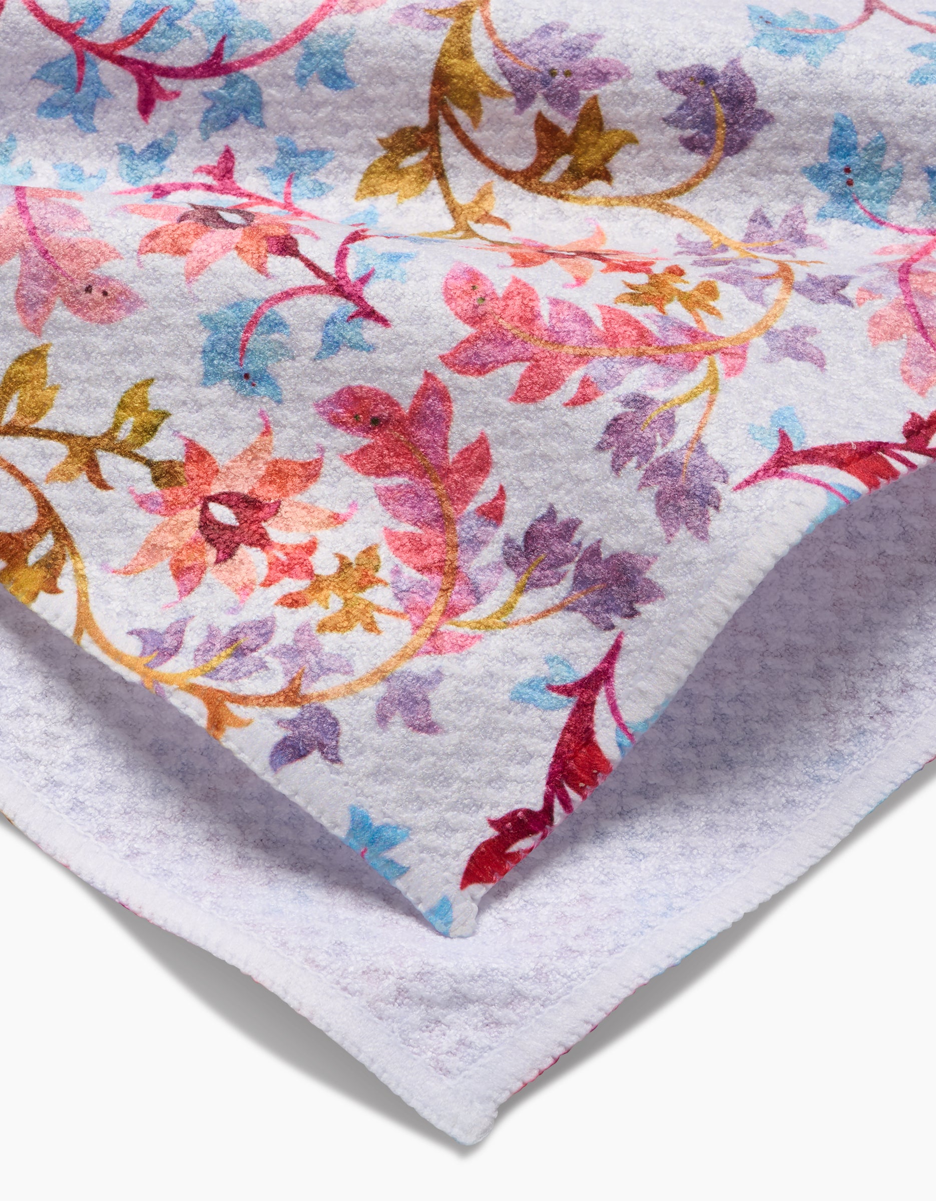 A close-up of the Maayan Alper-Swan Folk Tapestry towel shows its colorful floral pattern and a folded corner revealing the ultra-absorbent Geoweave fabric underside.