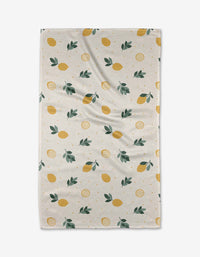 The Freshly Picked tea towel by Sara Mari features a beige recycled fabric with a textured finish, decorated with yellow lemons, green leaves, and orange dots in a repeating pattern and displayed slightly wrinkled.