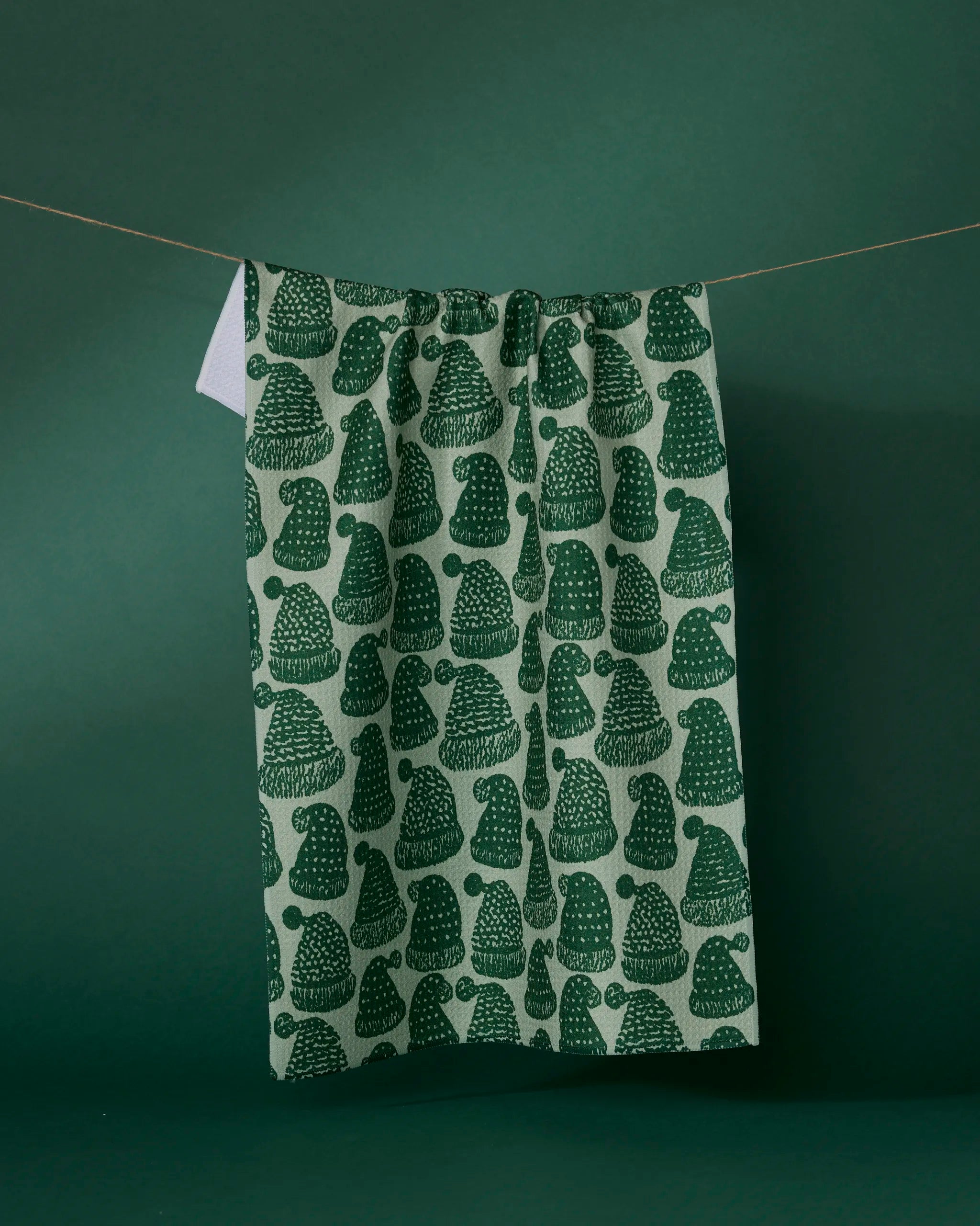 The Geometry Frostcap Green tea towel, ultra-absorbent and featuring a dark green mushroom pattern, hangs on a clothesline against a matching green background.