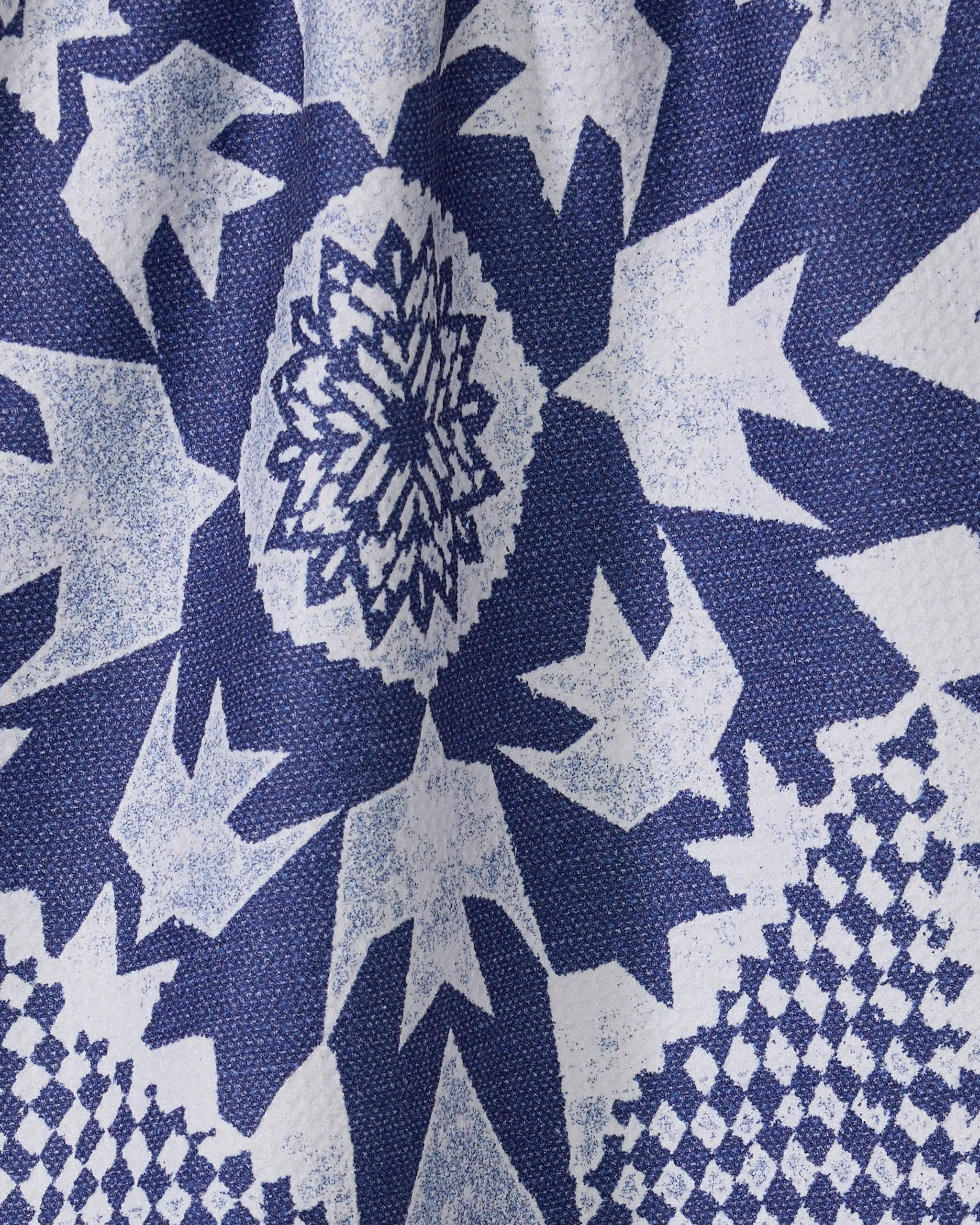Close-up of Geometry’s Froststar kitchen towel featuring a blue and white geometric star pattern with jagged edges and a central floral motif, made from textured recycled materials.