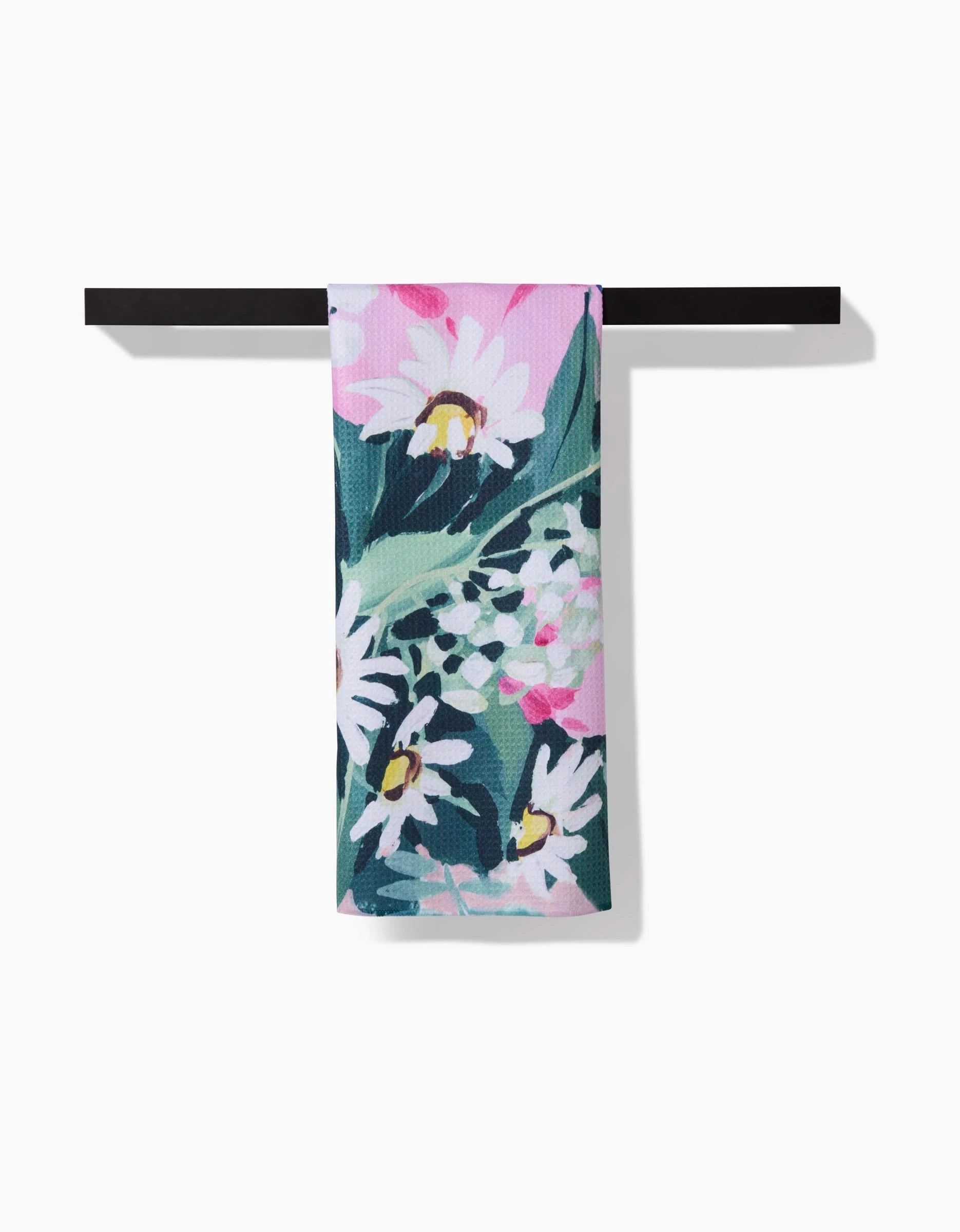 A Garden Bouquet tea towel by Ania Zwara Art, featuring floral patterns in pink, white, and green, hangs over a black bar. Made from ultra-absorbent Geoweave fabric, it stands out against the plain white background.