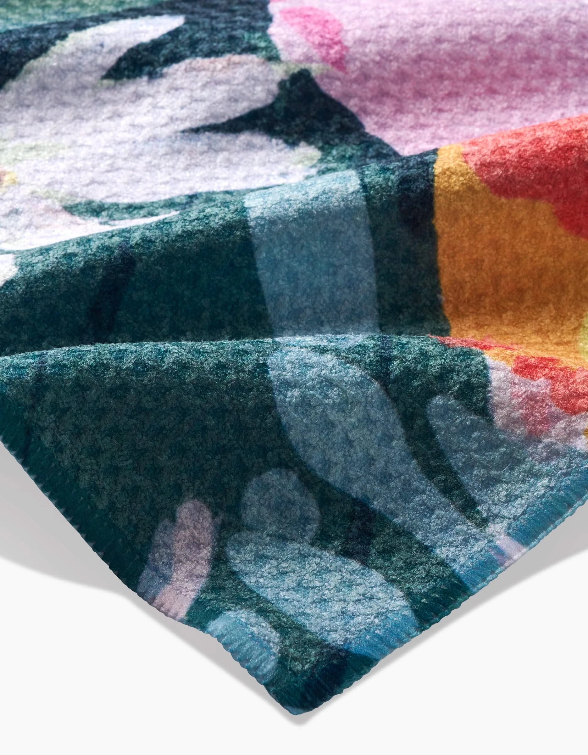 A close-up of Ania Zwara Arts Garden Bouquet shows its soft, ultra-absorbent Geoweave fabric with a fuzzy texture and a vibrant floral pattern in green, pink, white, orange, and blue. The material is folded to highlight its colorful design.