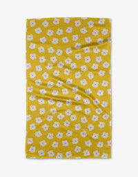 The Sara Mari “Garden Crush” tea towel features a yellow base with scattered small white flowers with orange centers. Laid flat, its gentle folds highlight its eco-friendly recycled material construction.