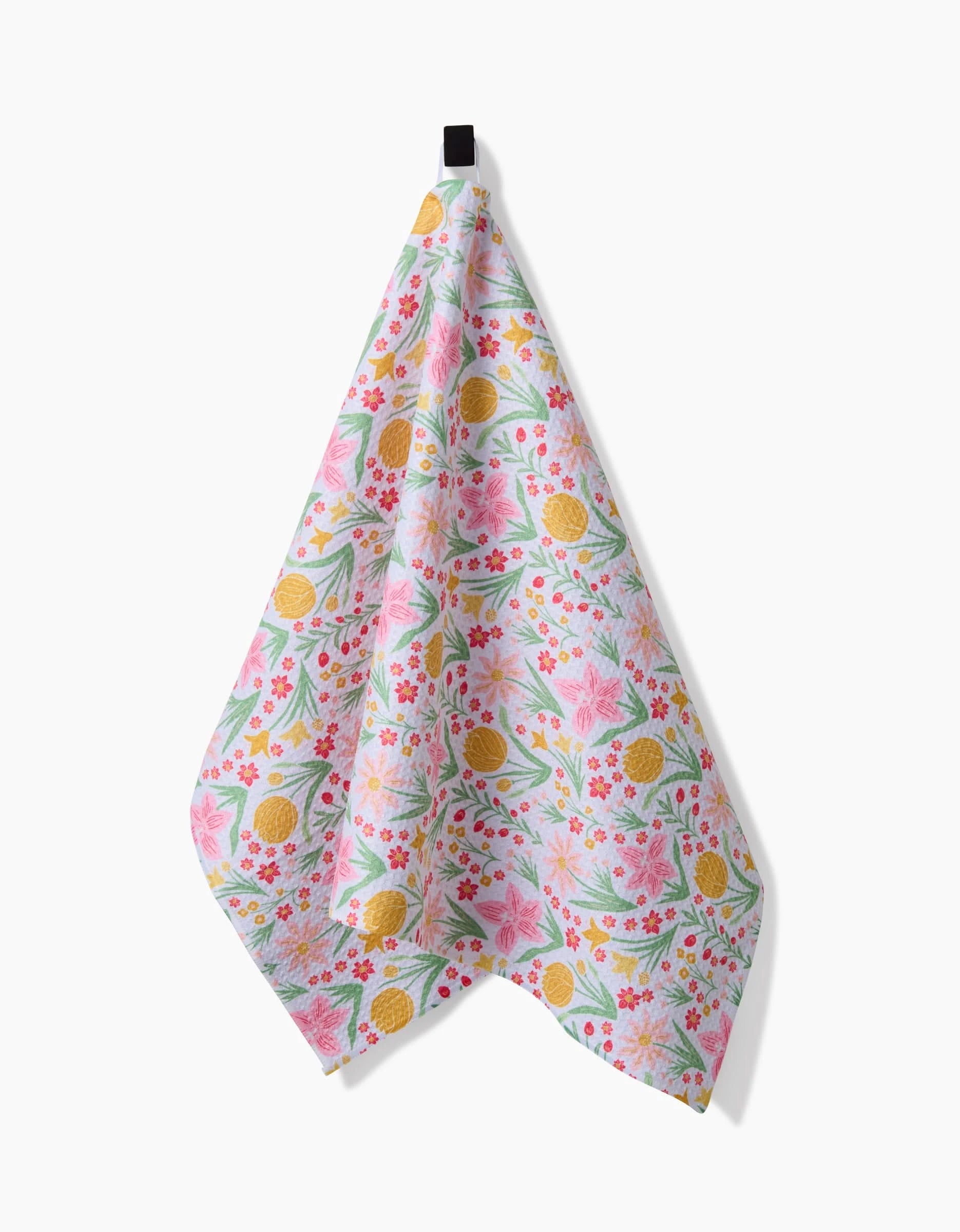 The Garden of Light tea towel by Danelys Sidron features vibrant floral and pineapple patterns in pink, yellow, and green on premium Geoweave fabric, hanging from a black loop against a white background.
