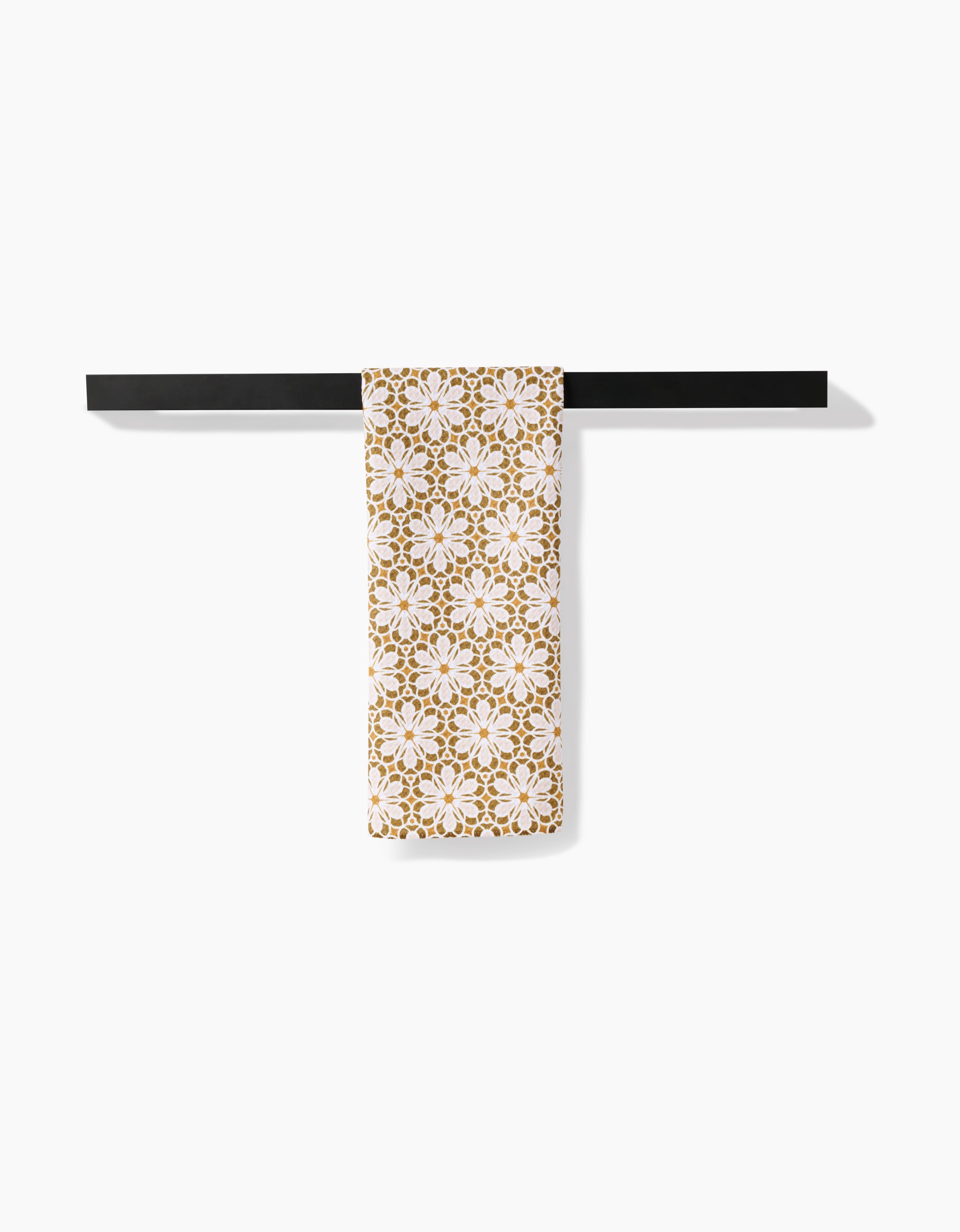 The Marta Harvey Geometric Flower white tea towel, featuring a gold floral design and crafted from Geoweave fabric, is draped over a black towel bar against a plain white background.