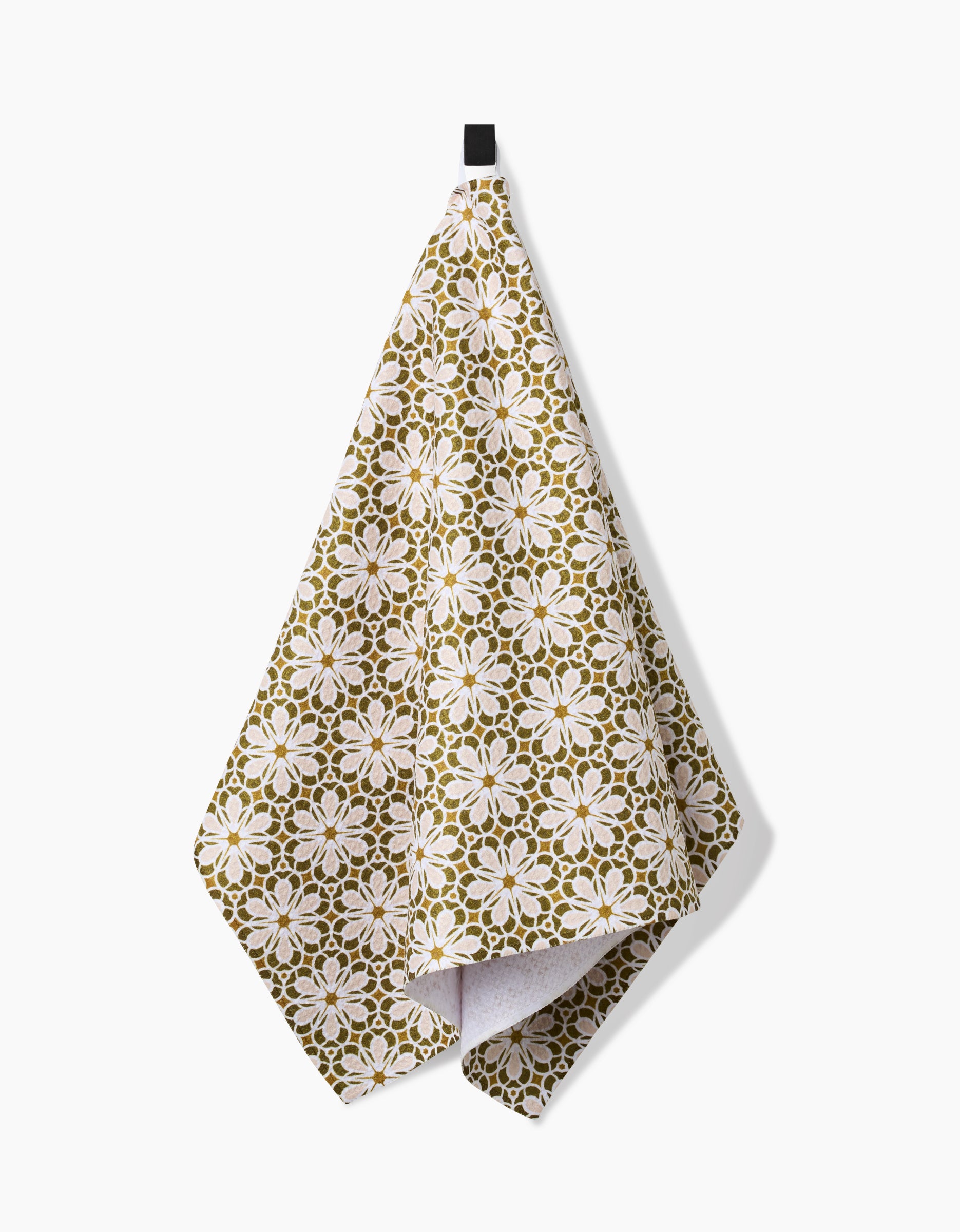 The Marta Harvey Geometric Flower tea towel in green and white, made from recycled materials, hangs from a black hook against a plain white background.
