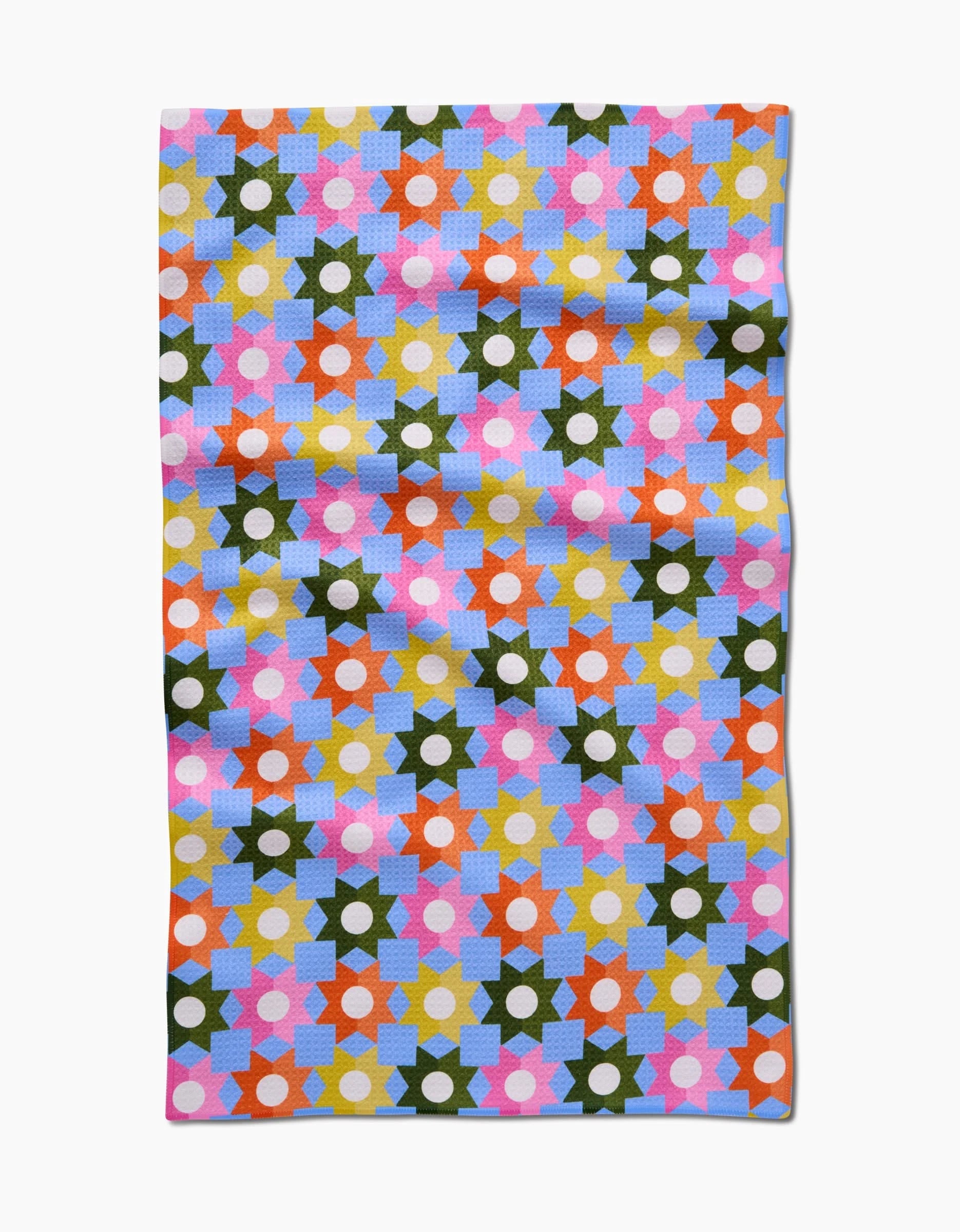 The Geometric Garden cloth by Megan Roy features a vibrant geometric pattern of stars and hexagons in pink, orange, yellow, green, blue, and white on a light background. Made from ultra-absorbent Geoweave fabric and shown laid flat with slight wrinkles.