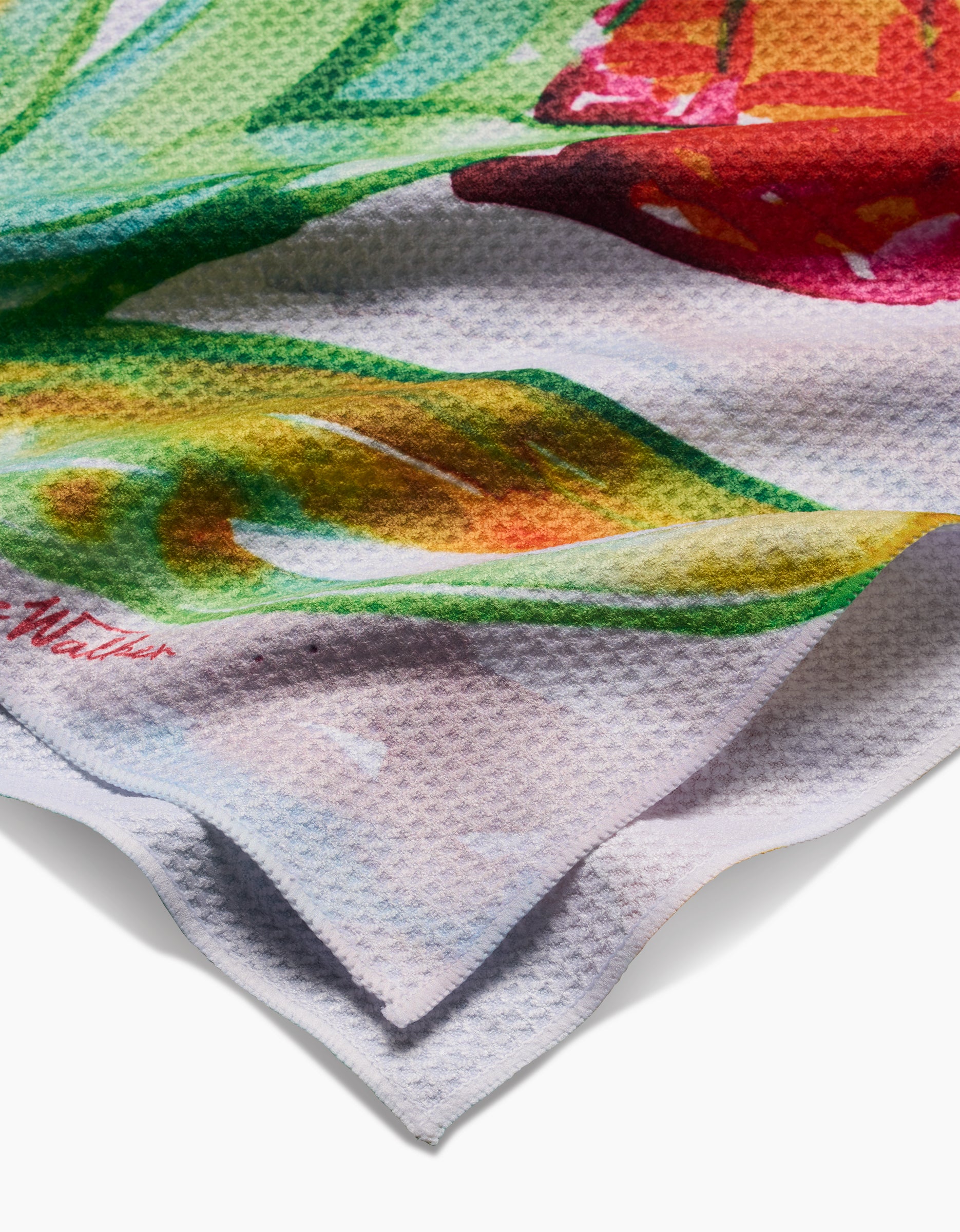 A close-up of the Skye Walker Ginger Geoweave fabric displays its vibrant green, yellow, and red abstract print. The ultra-absorbent cloth is slightly folded, highlighting its layered edges and textured surface.