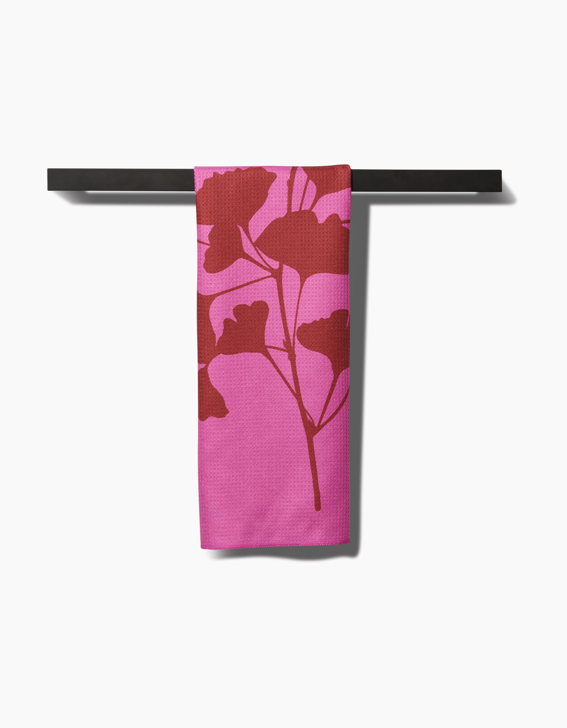 A PrintedPlant Ginkgo towel, featuring a bold red botanical print on pink ultra-absorbent Geoweave fabric, hangs neatly from a dark bar against a white background.