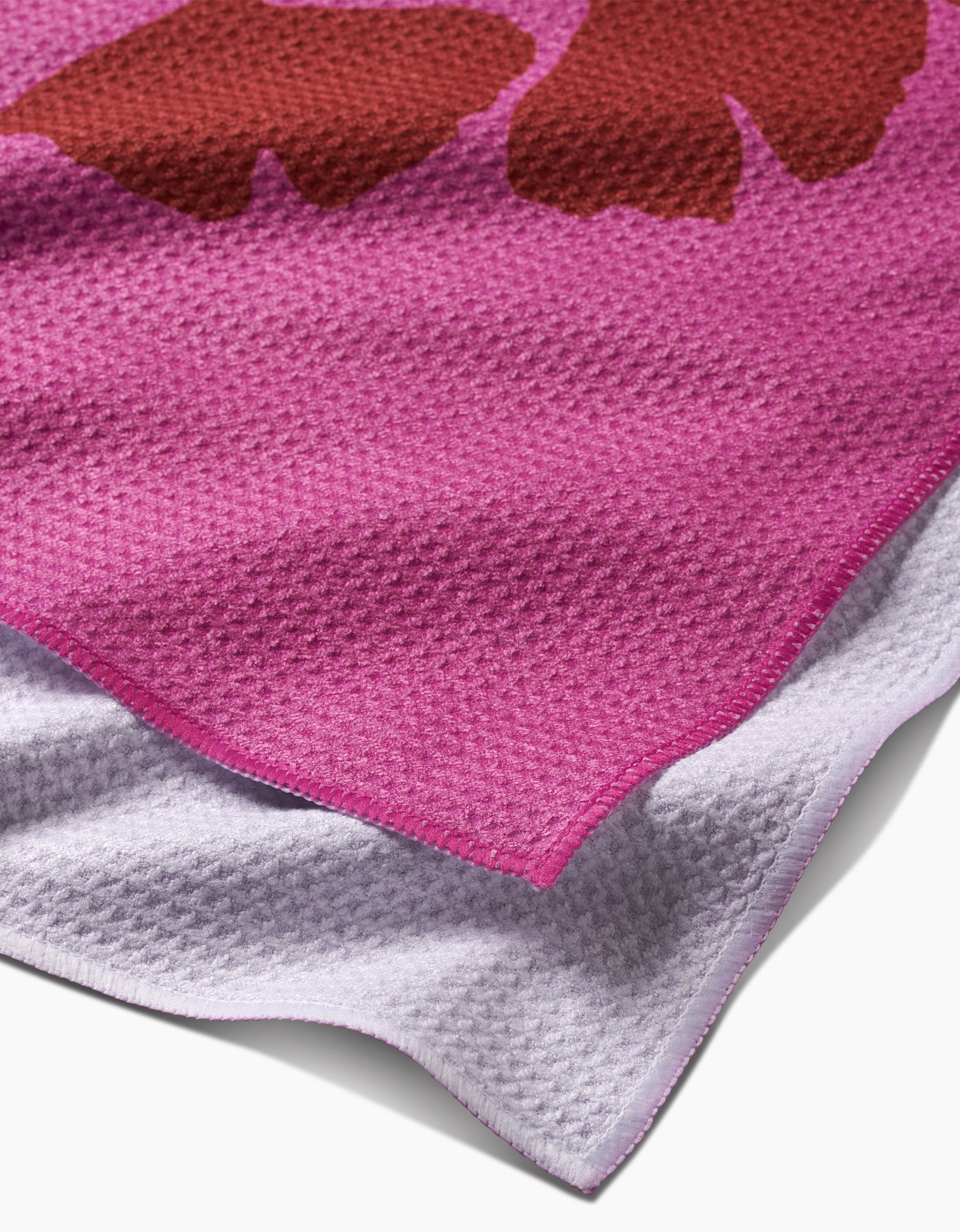 A close-up of PrintedPlant’s Ginkgo towel shows its pink and purple Geoweave fabric with a brown abstract shape and a neat pink border, highlighting the ultra-absorbent edge.