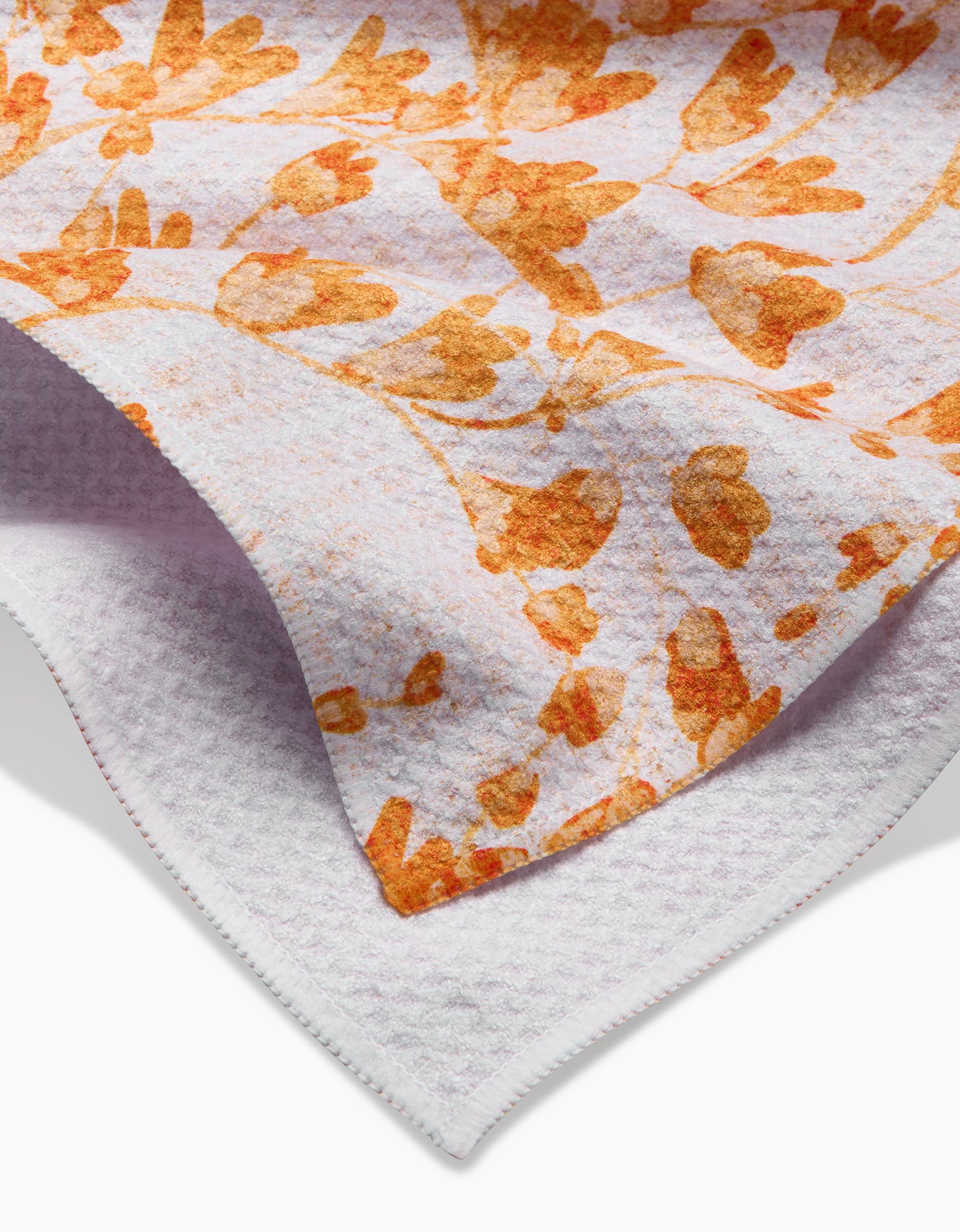 A close-up of Pascale Dilger’s Golden Grassland Tea Towel, featuring an orange floral pattern on white Geoweave™ fabric. The textured towel is slightly folded, showcasing its thickness and layers.