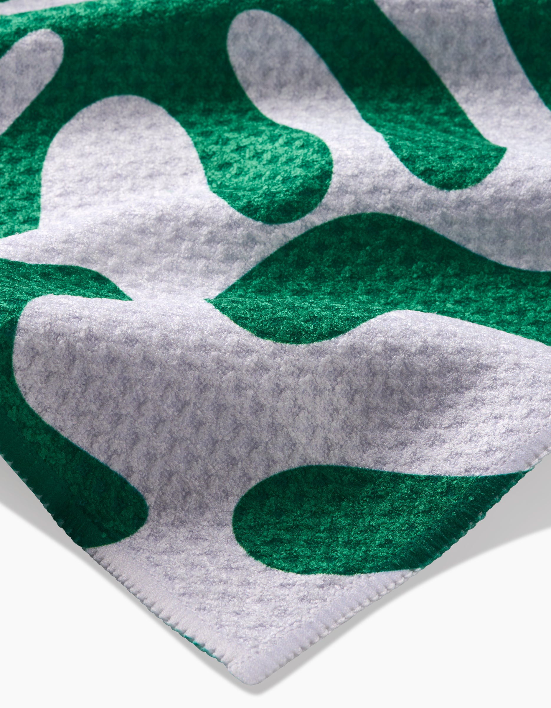 A close-up of the Green Afternoon towel by Marina Solodka, showing its bold abstract green and white pattern on ultra-absorbent, textured fabric.