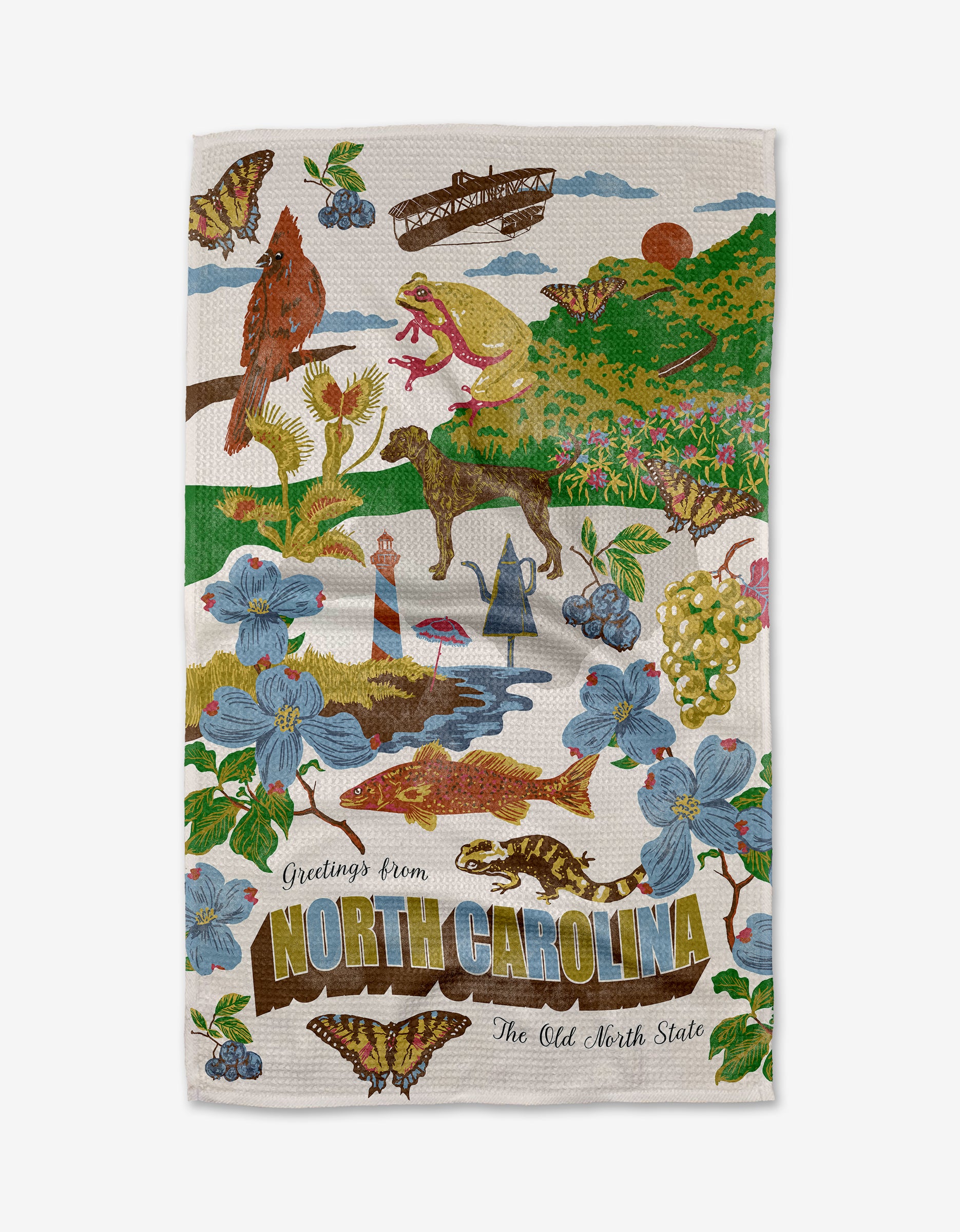 The Geometry "Greetings From North Carolina" kitchen towel features NC symbols—cardinal, dogwood, lighthouse, grapes, butterflies, trout, salamander, Blackbeard’s ship—and “Greetings from North Carolina, The Old North State” text. Made from recycled materials.