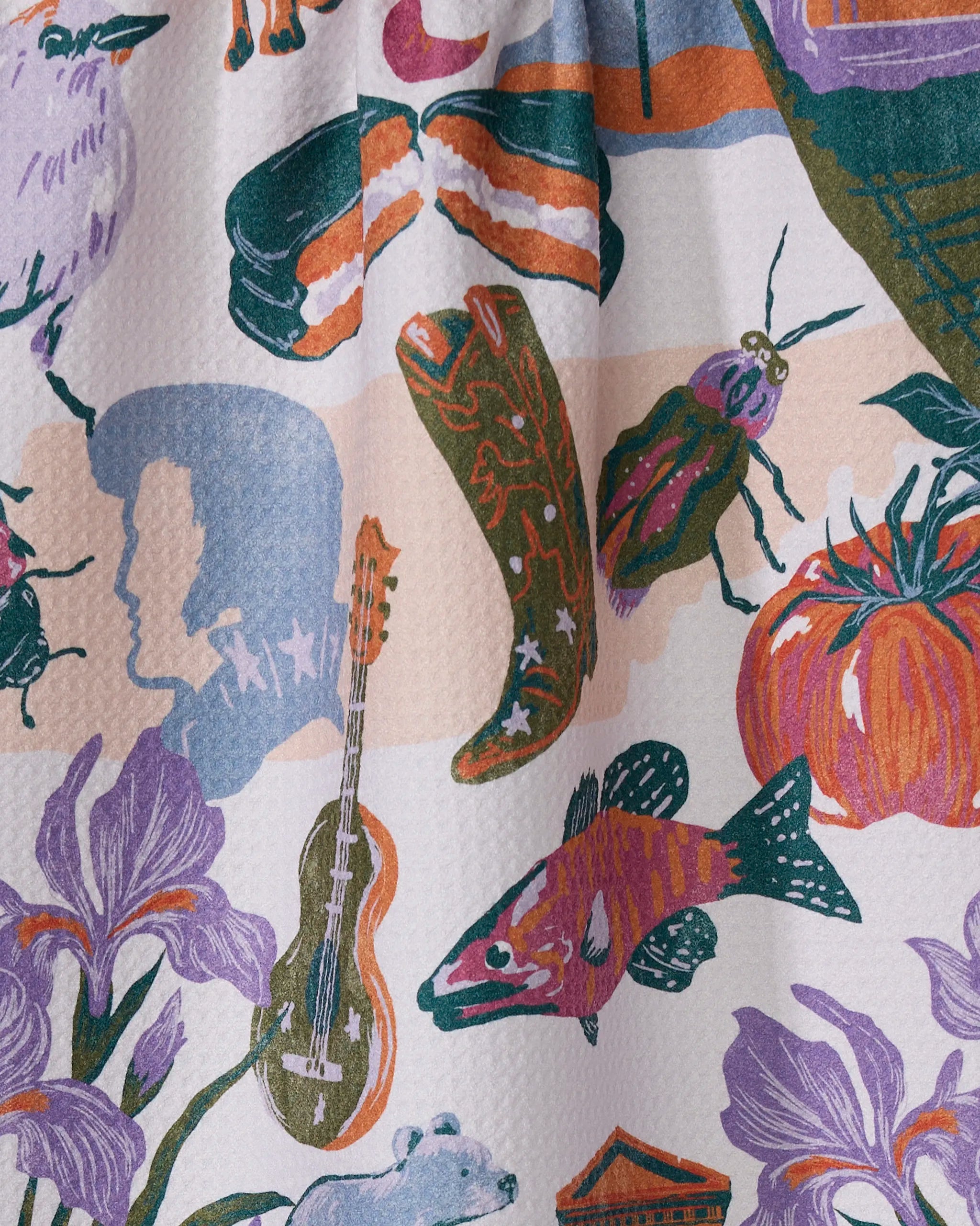 The Geometry "Greetings From Tennessee" tea towel features a colorful illustration of cowboy boots, a guitar, sushi, and more on a textured white surface. Made from recycled materials, it dries quickly.