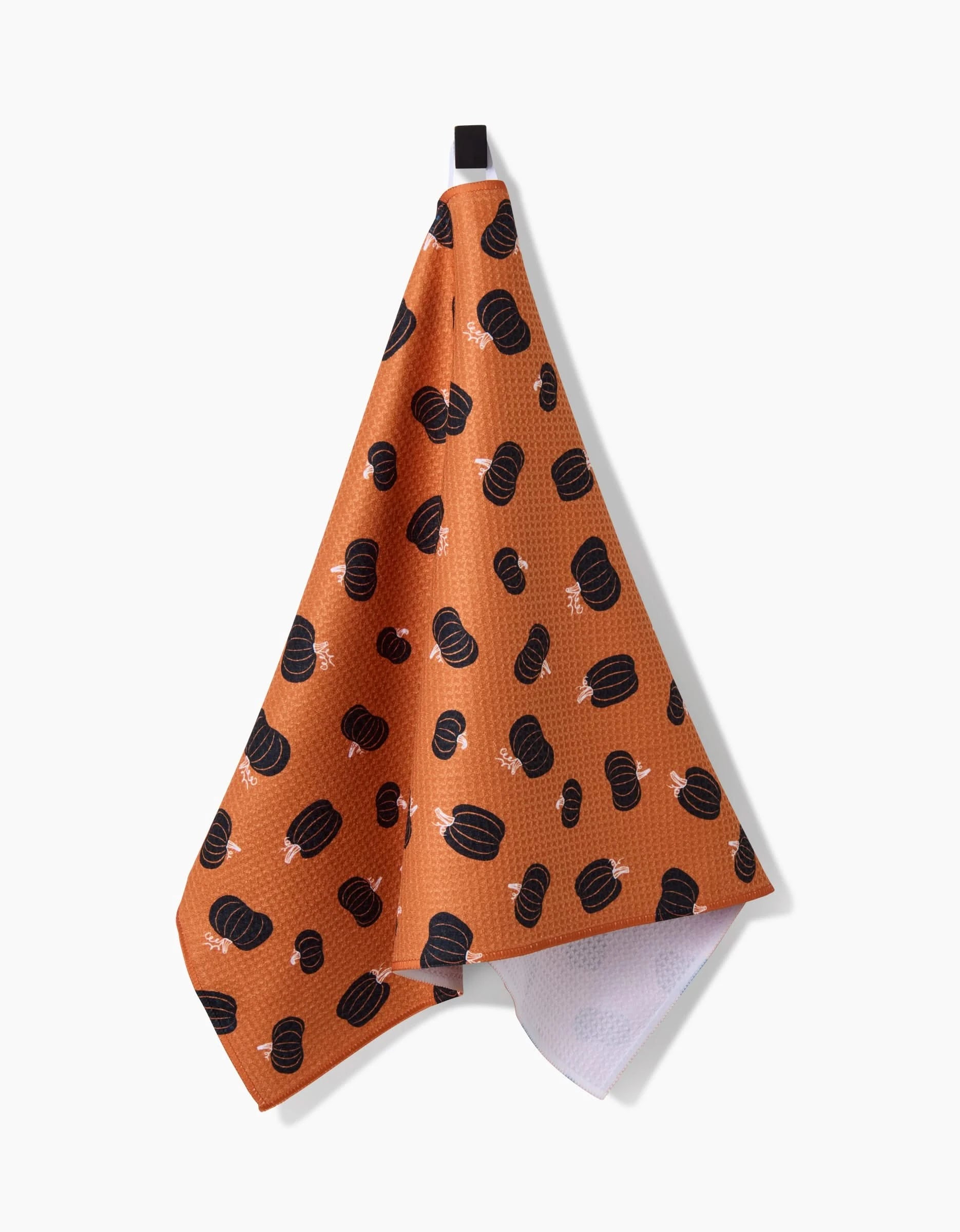The Halloween Black Pumpkins tea towel by Hufton Studio, featuring black pumpkin and white bone patterns on ultra-absorbent orange fabric, hangs from a black loop against a plain white background.
